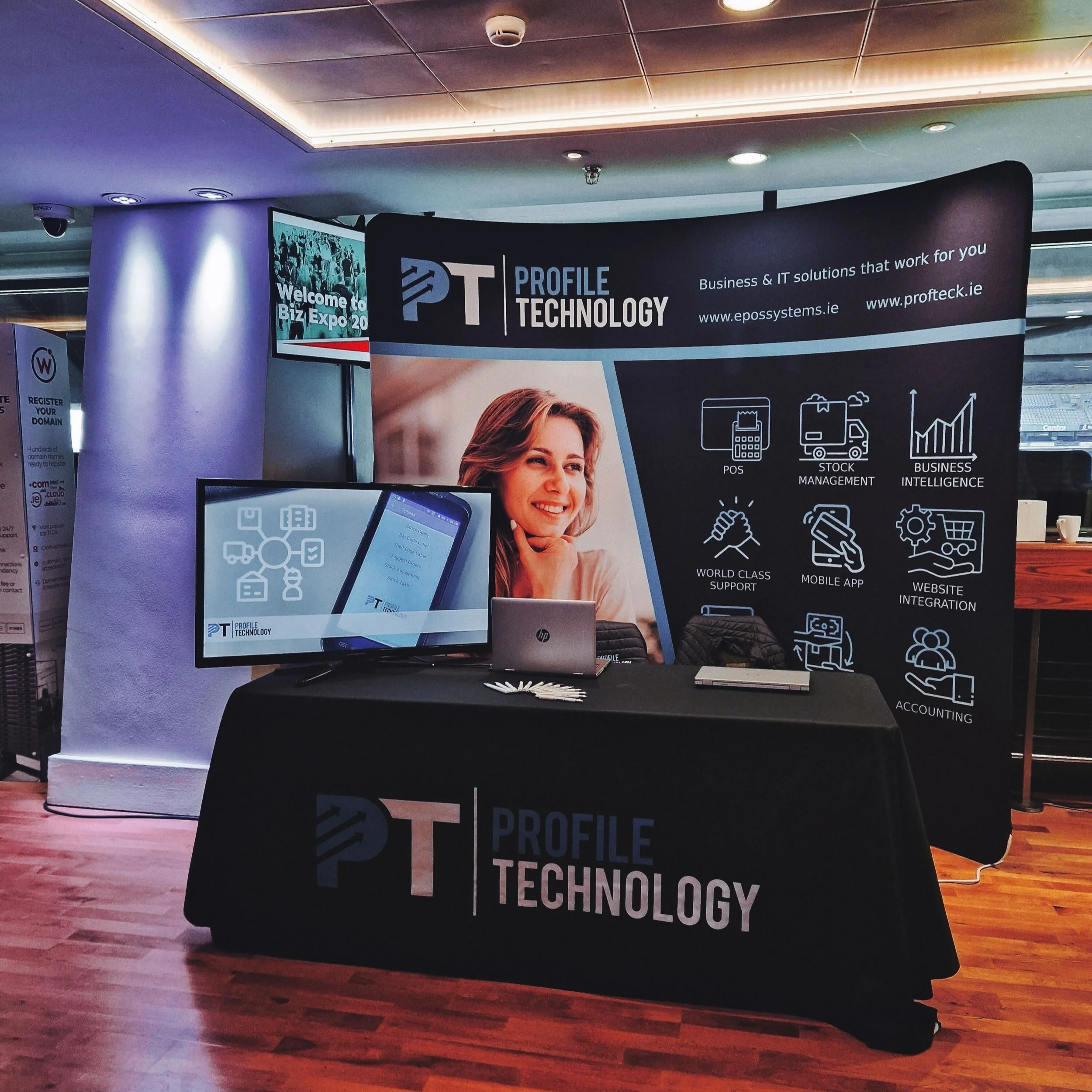 Trade show booth for Profile Technology with a black tablecloth, a large informational banner, a computer monitor, and promotional materials, promoting IT solutions and services.