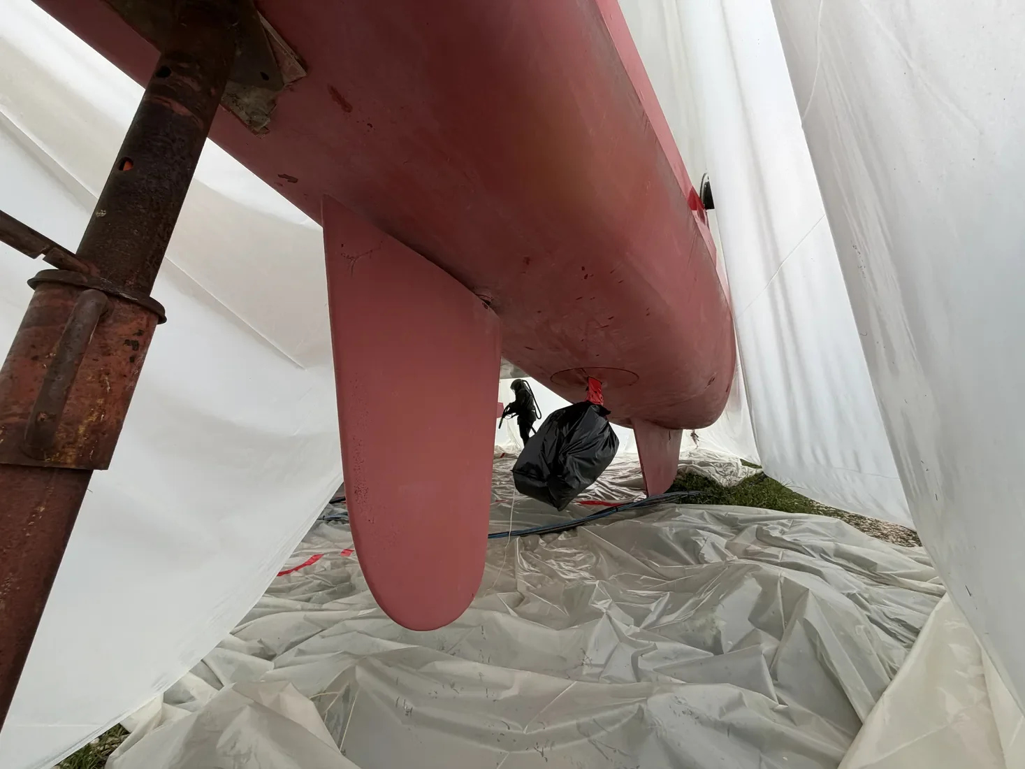 Aérogommage en cours sous encapsulage sur coque antifouling rouge de catamaran