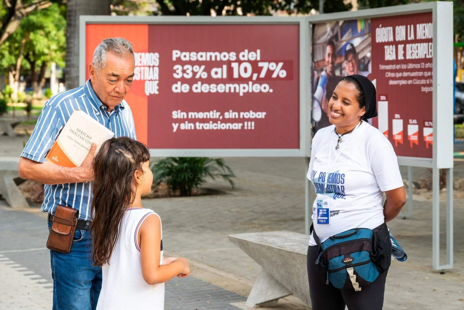 COLOMBIA 2023. Public accountability exhibition of the Cúcuta municipal administration.

20 December 2023. Cúcuta, Norte de Santander, Colombia. A municipal outreach worker speaks with an older man and a young girl beside large-format display panels 