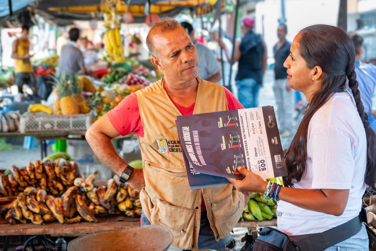 COLOMBIA 2023. Outreach at the Mercado Público de San Luis, Cúcuta.

20 December 2023. Mercado Público de San Luis, Cúcuta, Norte de Santander, Colombia. A municipal outreach worker shows a results poster from Mayor Jairo Yáñez's 2020 to 2023 adminis
