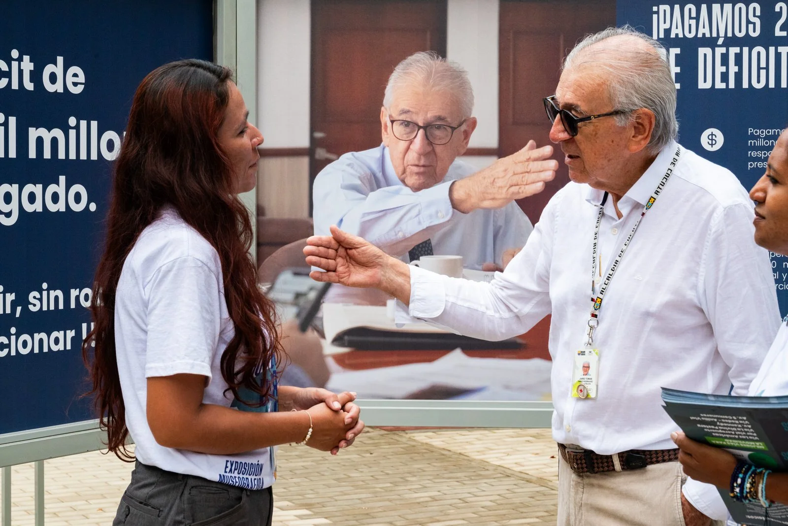 COLOMBIA 2023. Public accountability exhibition of the Cúcuta municipal administration.

20 December 2023. Cúcuta, Norte de Santander, Colombia. Mayor Jairo Yáñez speaks with two municipal outreach workers in front of large-format display panels from