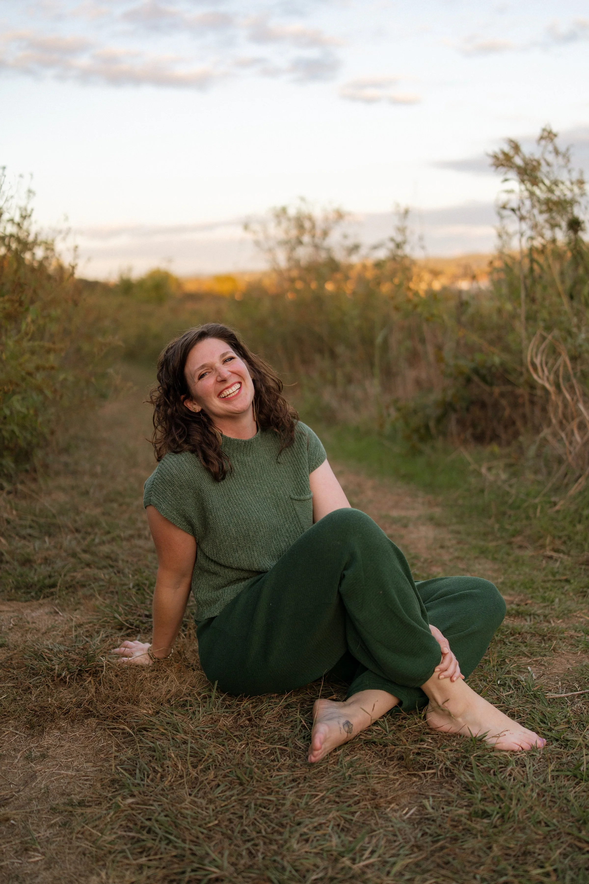 Leslie Greathouse sitting in a meadow at golden hour, laughing with her face turned upward
