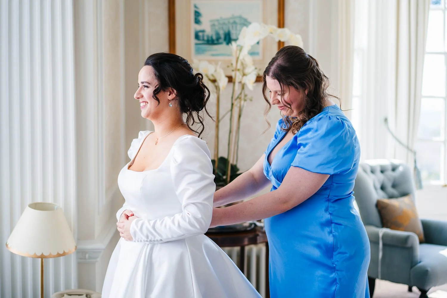 hedsor-house-wedding-bridesmaid-helping-put-brides-dress-on.jpg
