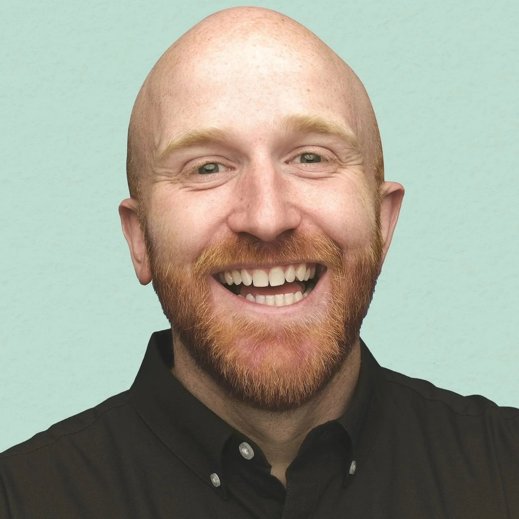 A headshot of a smiling man with a beard and mustache, wearing a black collared shirt, against a light-colored background.