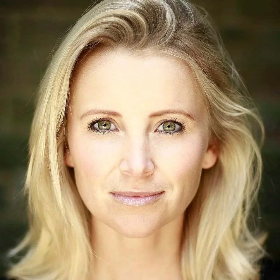 Close-up portrait of a woman with blonde hair and green eyes, smiling softly.