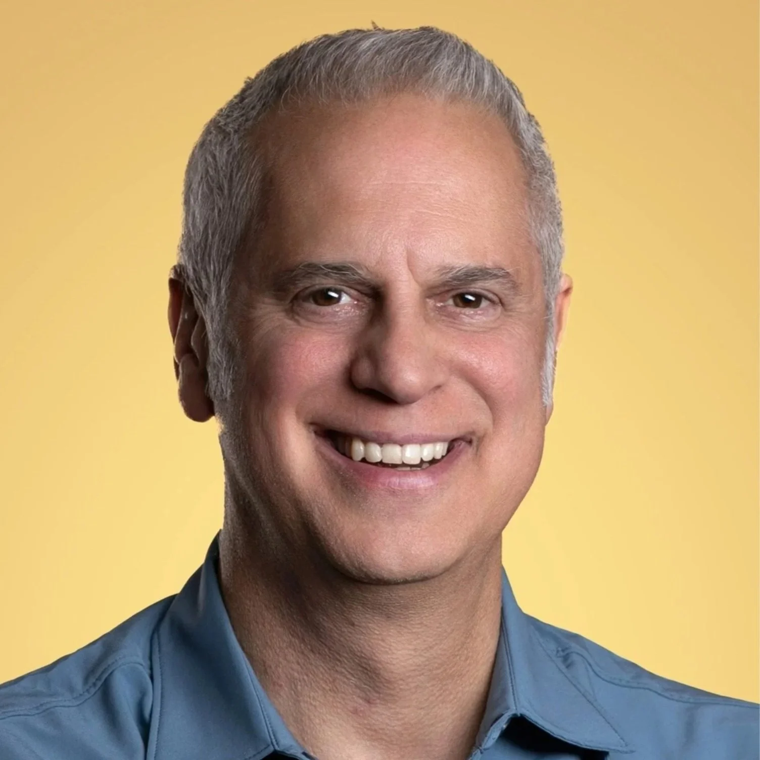 A smiling man with short gray hair, wearing a dark shirt, against a black background.