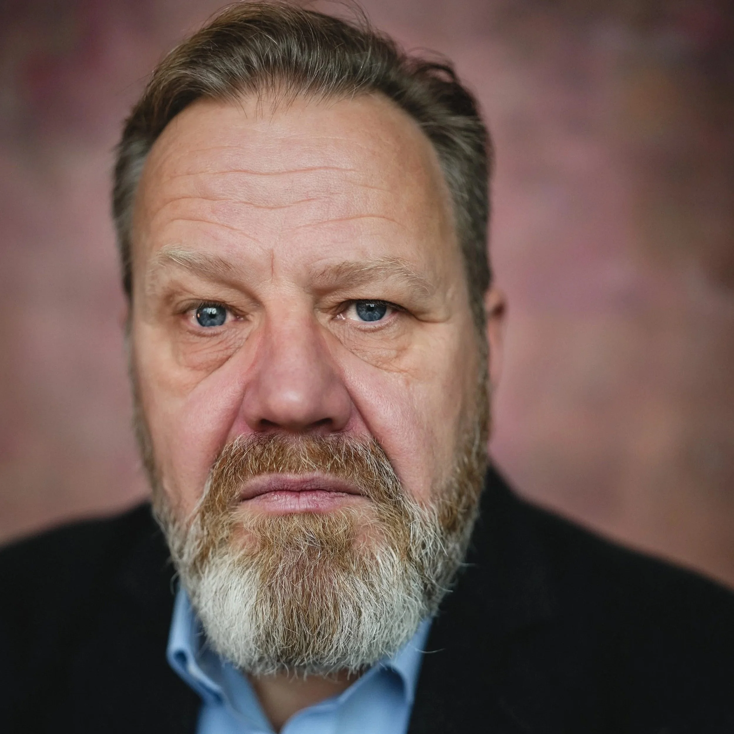 Close-up portrait of a middle-aged man with a beard and mustache, looking directly at the camera against a blurred background.