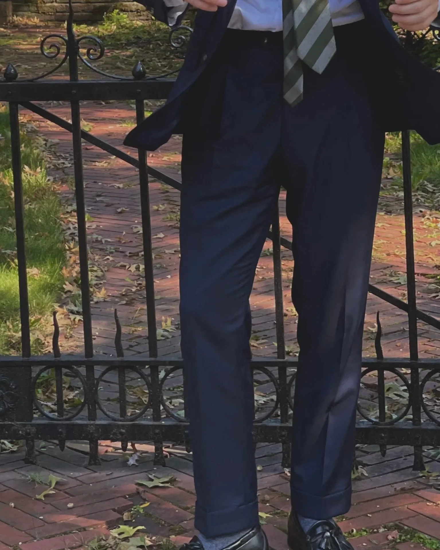 Navy pleated trousers with cuffs, worn at the natural waist