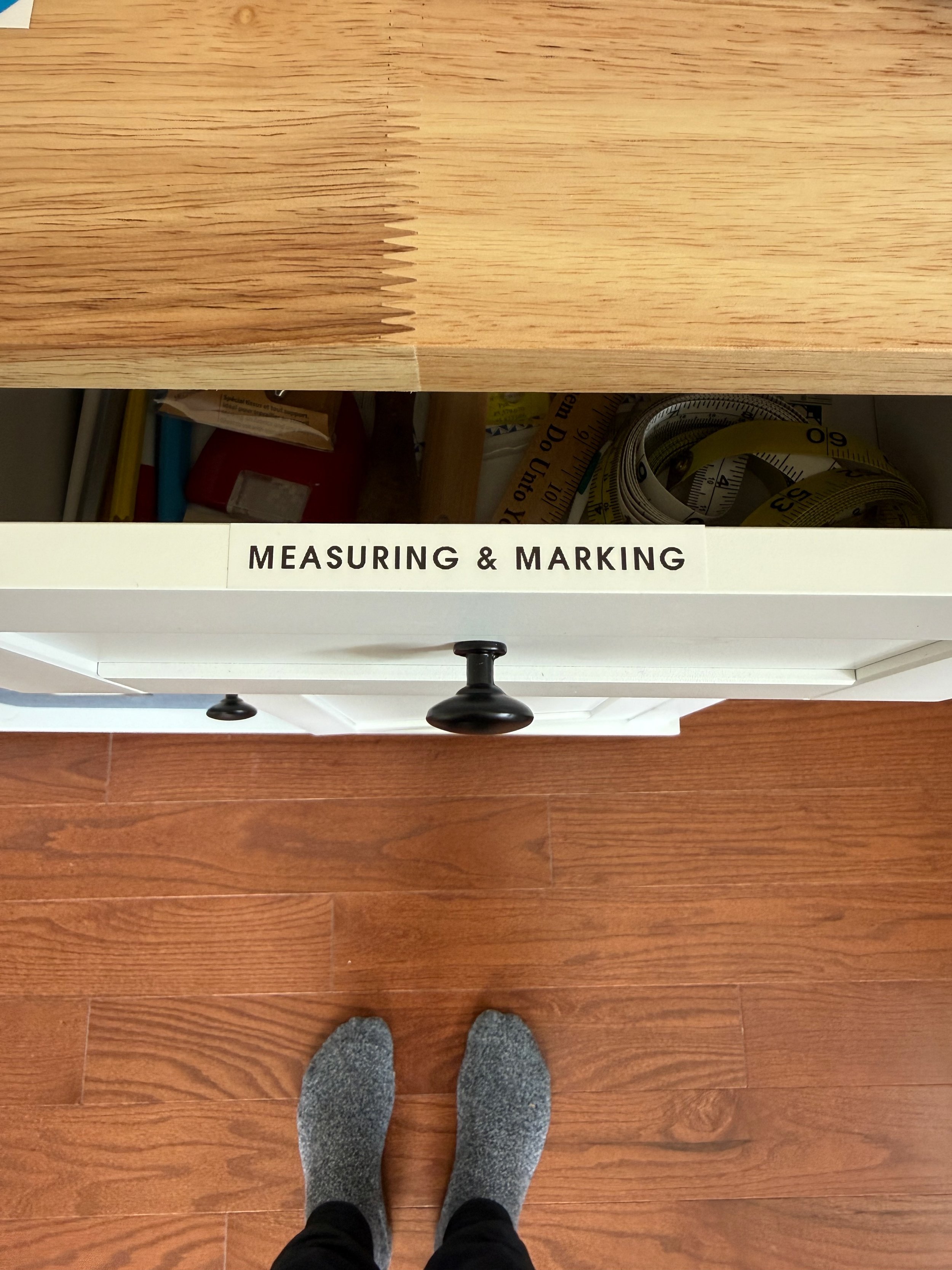 Measuring tapes and marking supplies grouped in a designated drawer, with a label identifying where they belong.