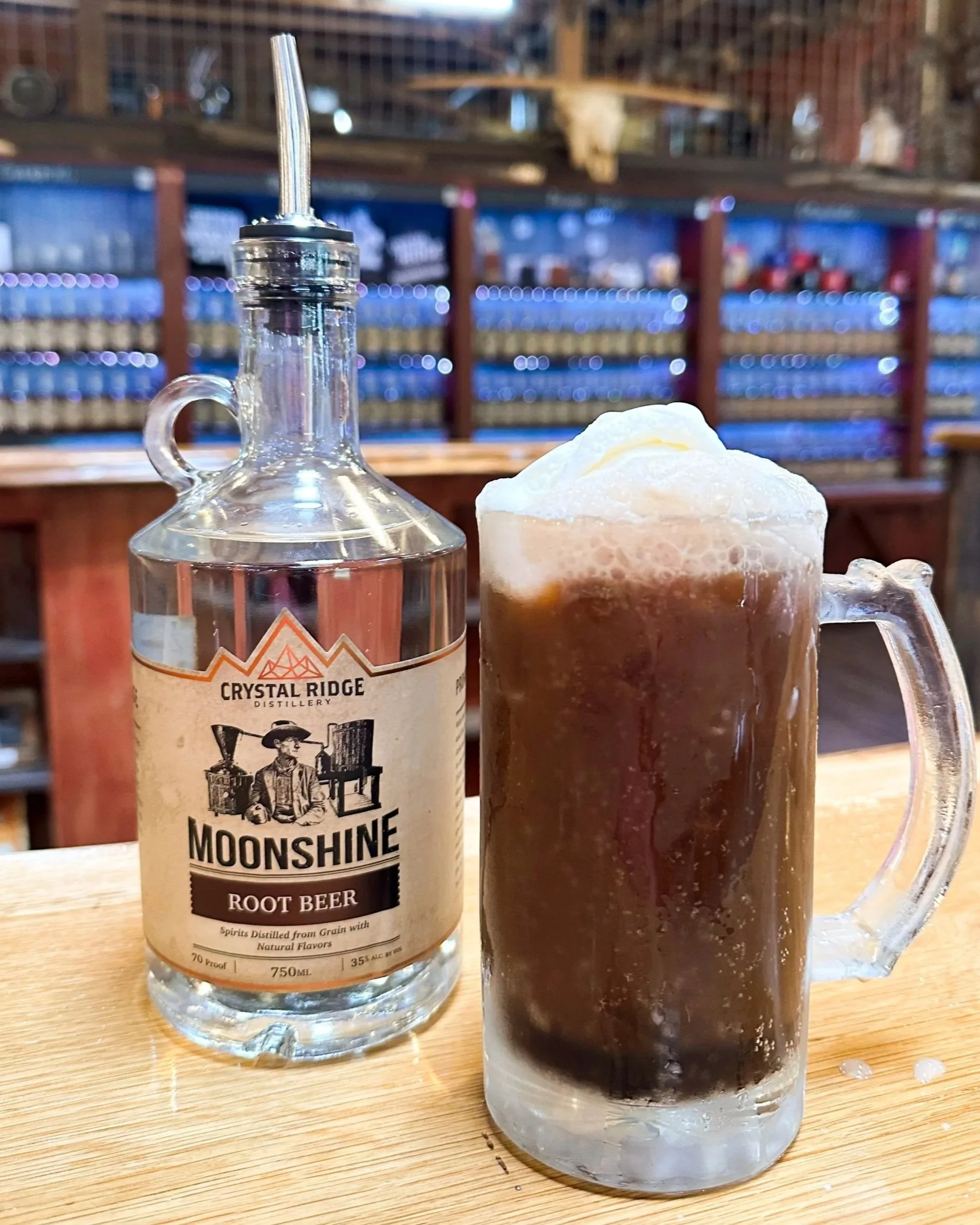 A bottle of Moonshine Root Beer flavored spirit next to a glass mug filled with root beer topped with foamy cream in a bar setting.