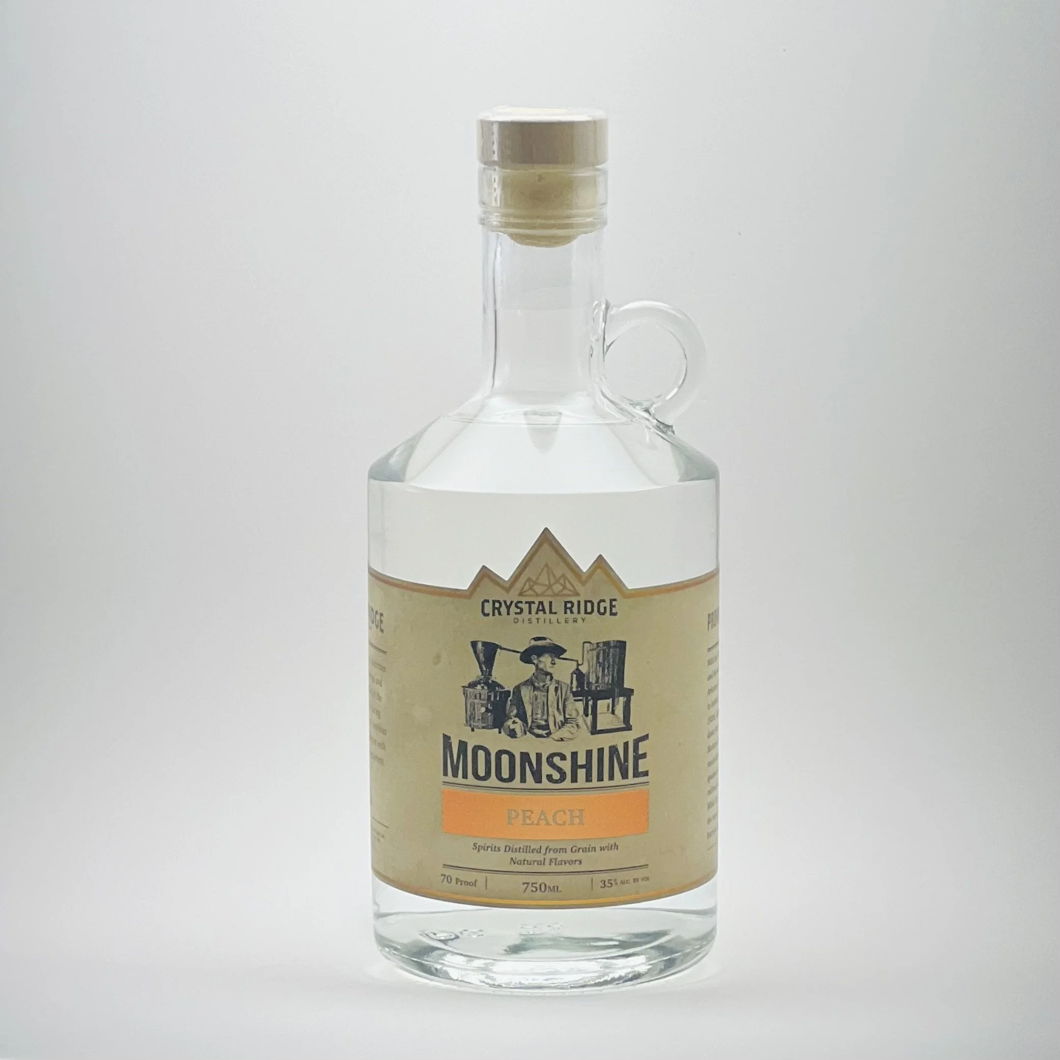 A clear glass bottle of Moonshine Peach by Crystal Ridge Distillery with a beige label, orange accent, and a mountain drawing, set against a plain white background.