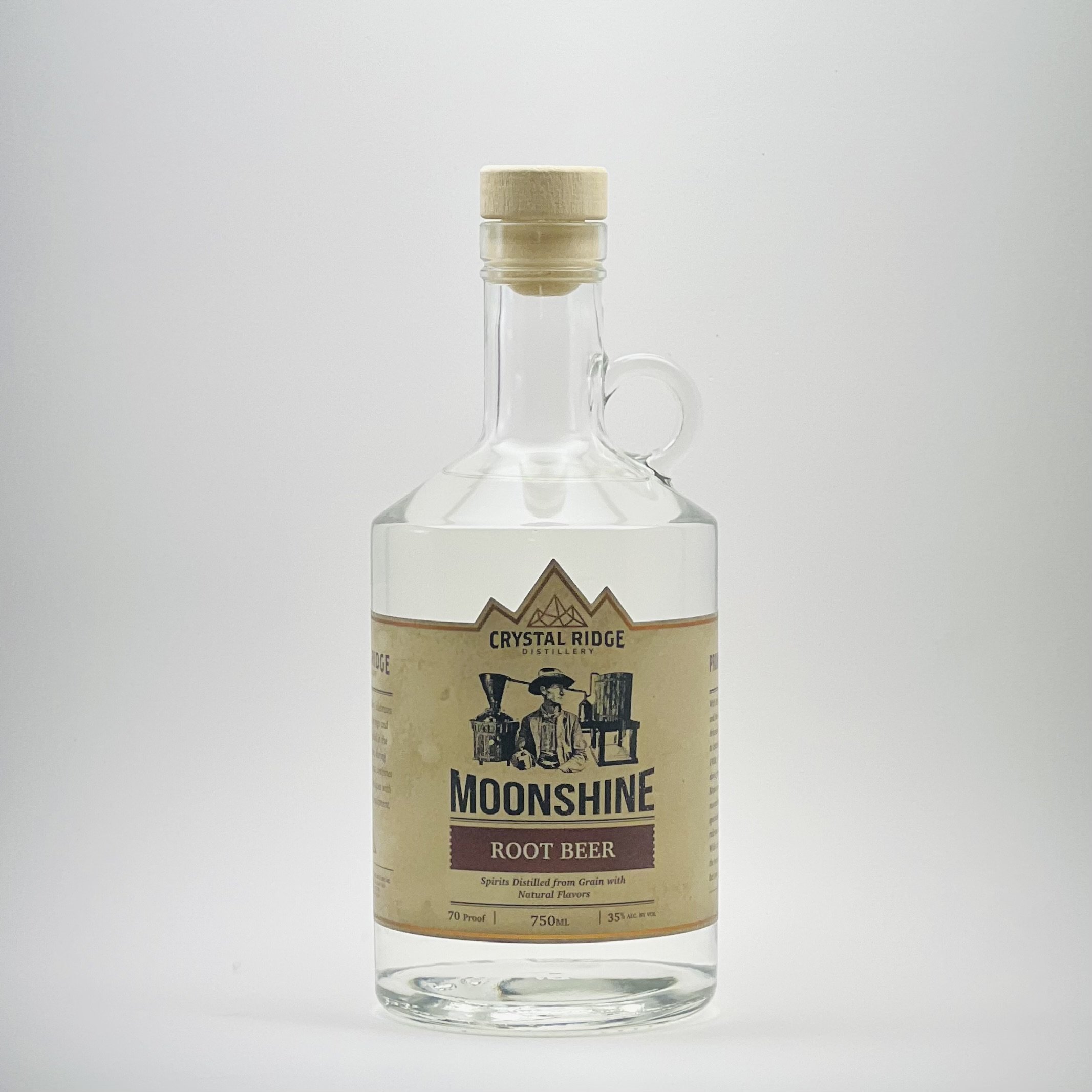 A clear glass bottle of Moonshine root beer with a beige label, black text, and a wooden cap, set against a plain white background.