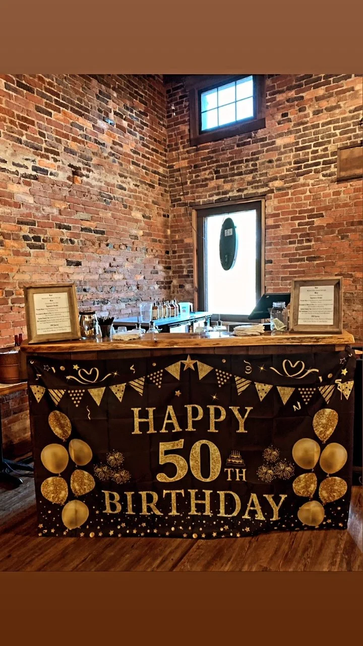 50th birthday celebration with balloons and decorations on a table in front of a brick wall and event bar.