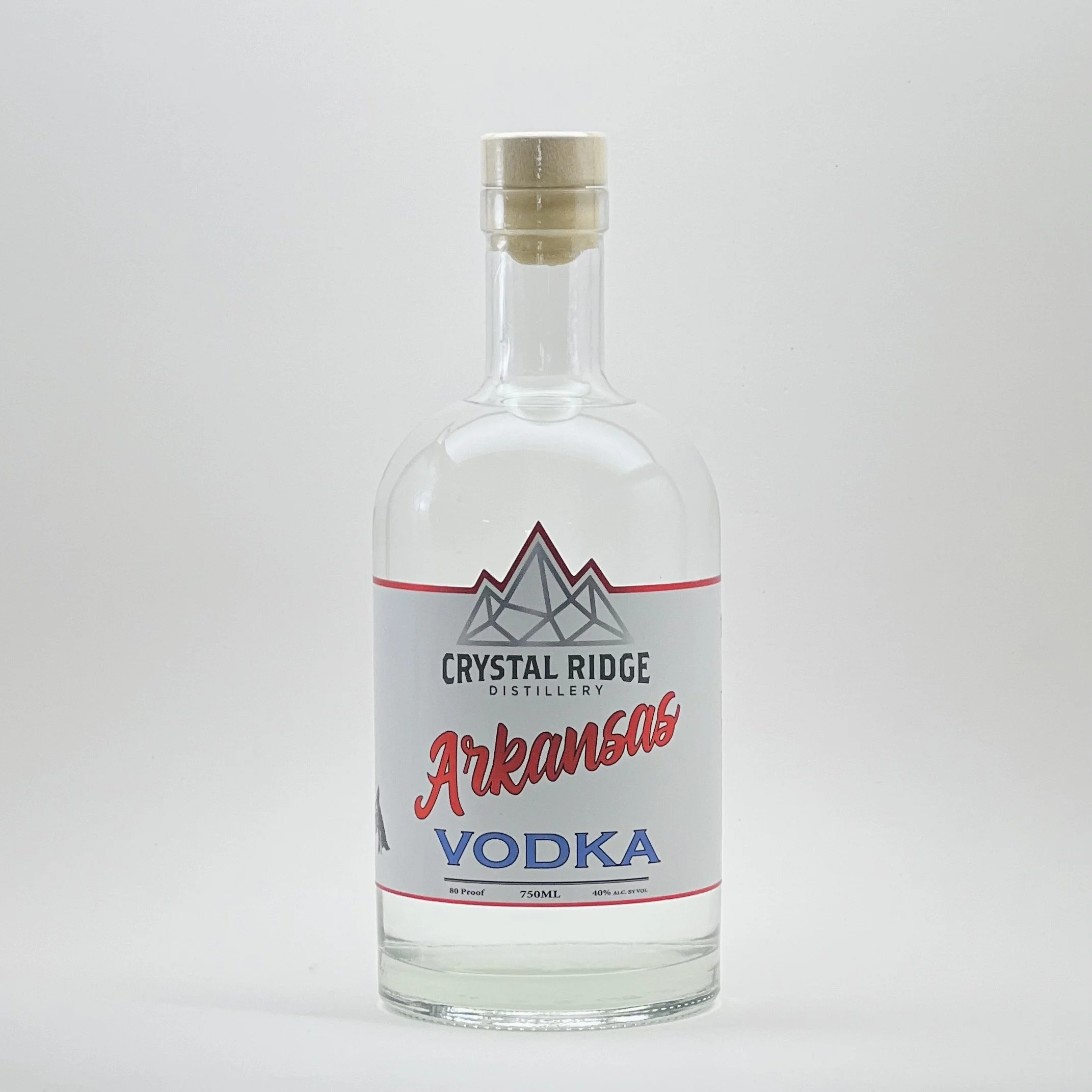 A clear glass bottle of Arkansas vodka with a beige cap and a label featuring a mountain graphic and the text 'Crystal Ridge Distillery Arkansas Vodka'.