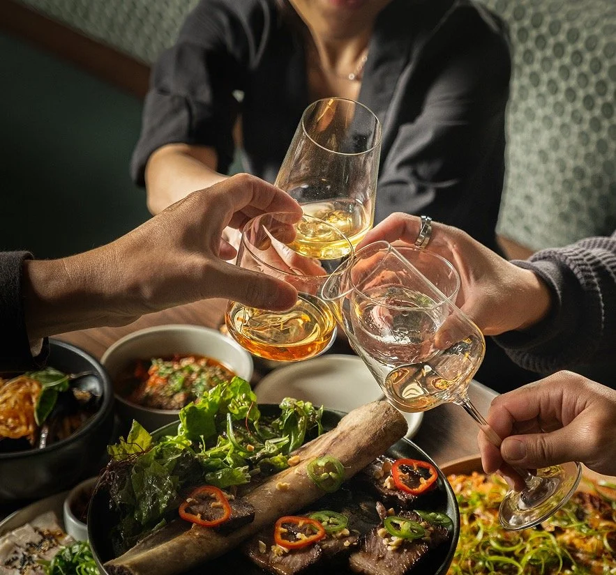 A group of people raising glasses in a toast over a table of shared Korean dishes at Hojokban