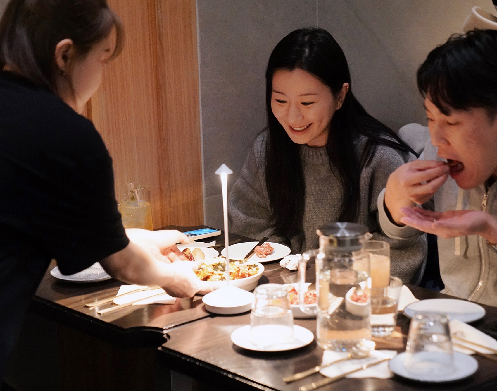 Two diners sharing food at a Hojokban NYC table while a server places fresh dishes in front of them