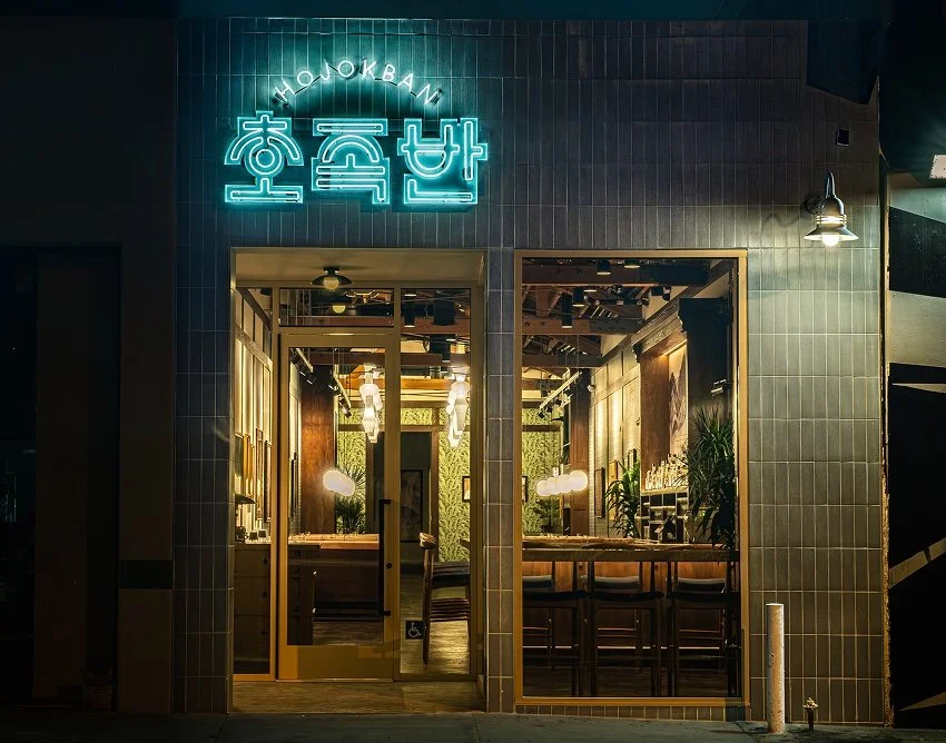 Hojokban restaurant exterior at night with illuminated Korean neon sign and the warm dining room visible through the front windows.