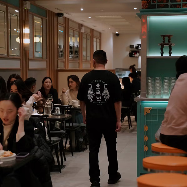 Man walking through a busy restaurant with several groups of people dining at tables.
