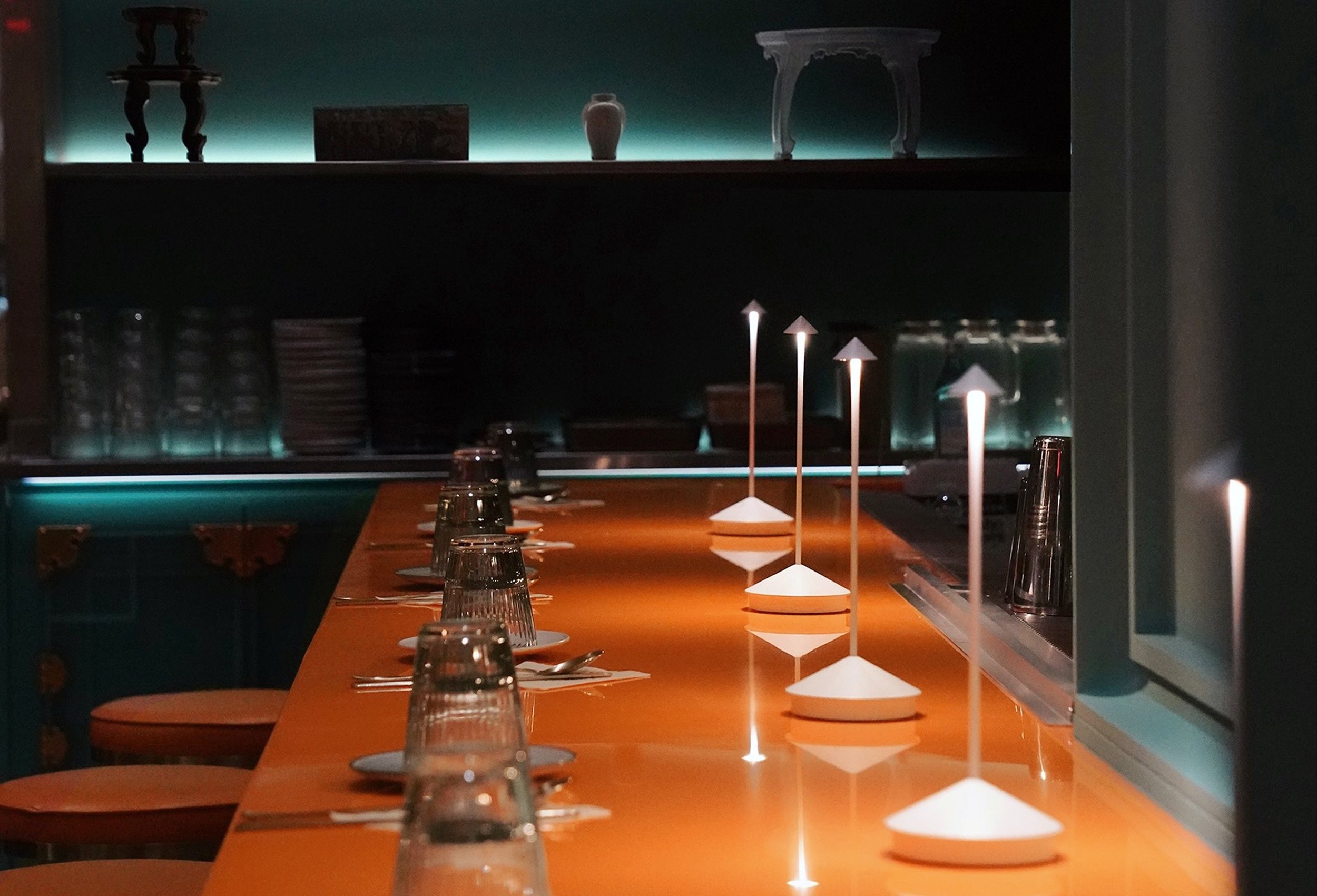 Interior of Hojokban featuring a modern orange bar counter, glassware place settings, and minimalist cone lamps in a dim, upscale dining space.
