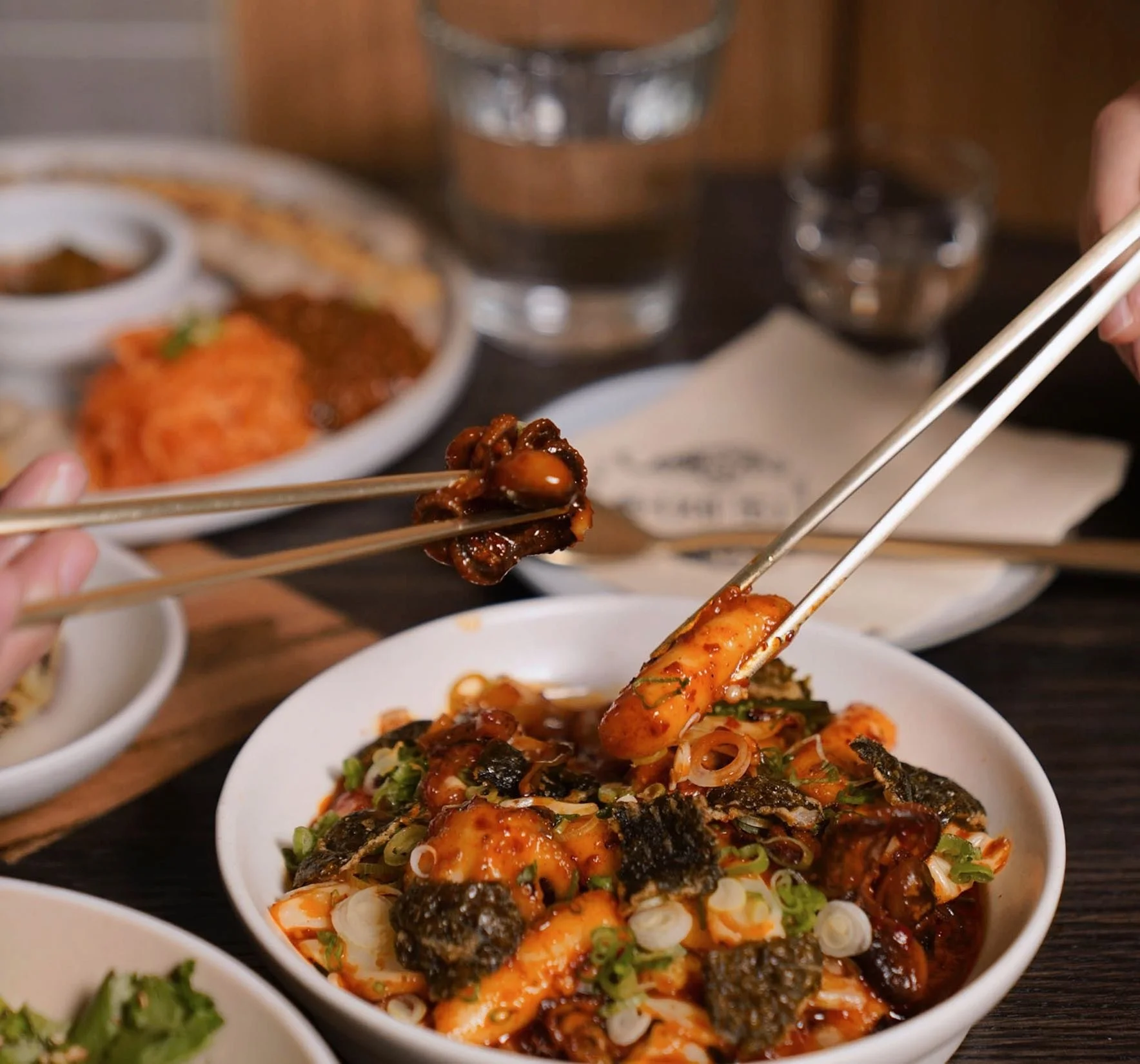 A close-up of chopsticks lifting food from a bowl on a Korean dining table at Hojokban