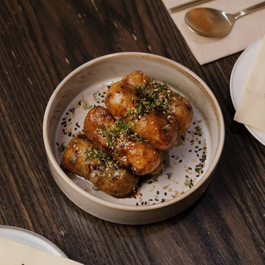 Fried eggplant coated in black garlic sauce, garnished with chive, sesame, and thyme on a ceramic dish