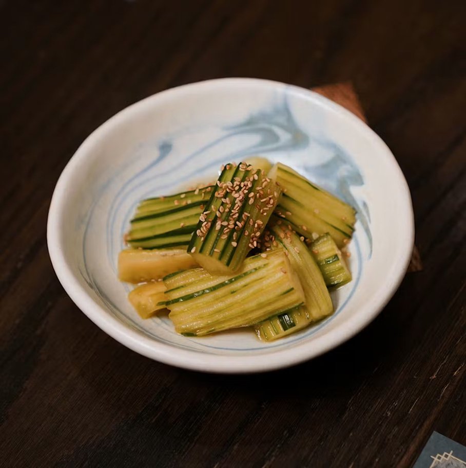 Close-up of soaked cucumber salad tossed in soy sauce and rice vinegar, topped with sesame seeds in a blue-swirled bowl