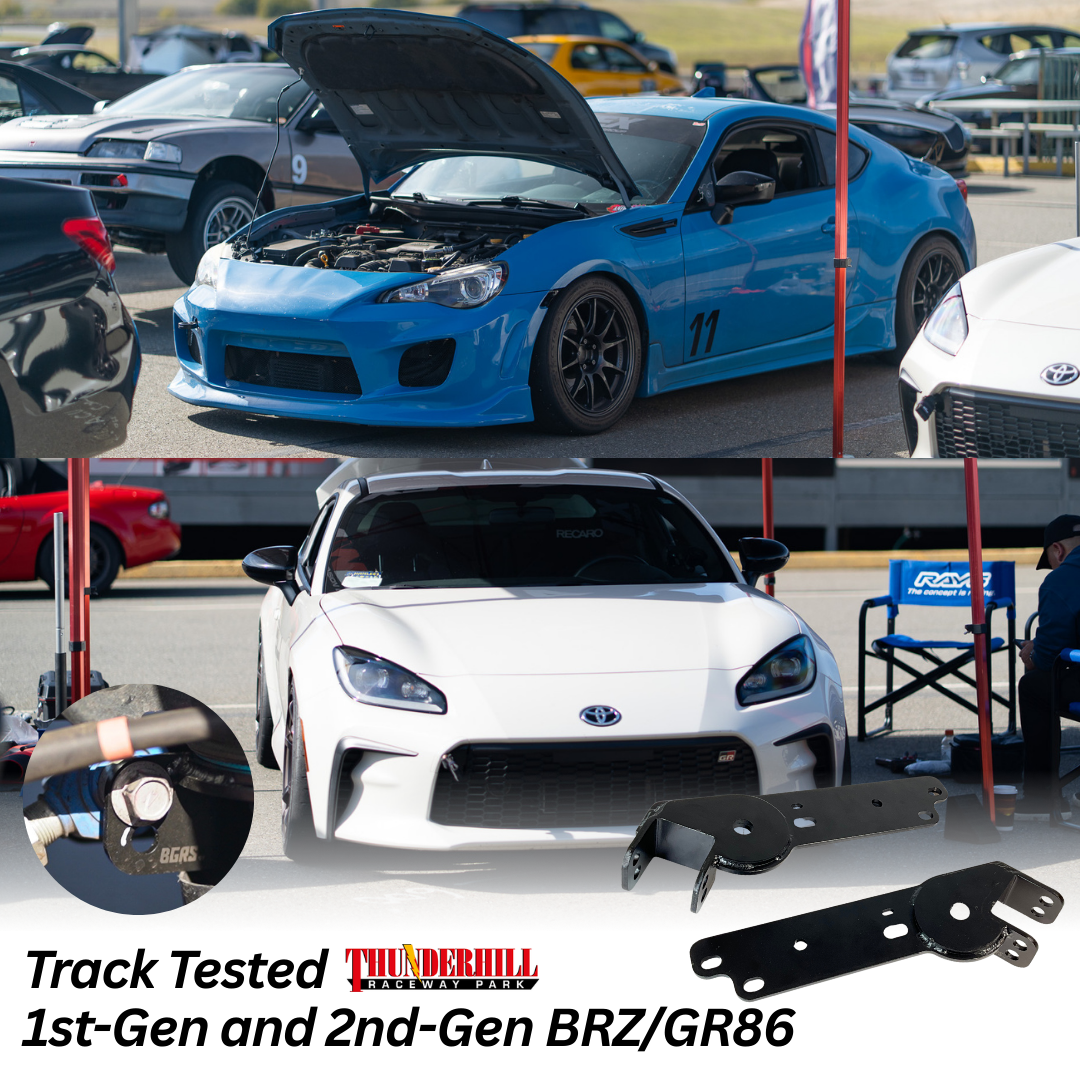 Two Toyota sports cars at a race track, a blue and a white model, with car parts and tools visible, under a red tent, with multiple other cars in the background.
