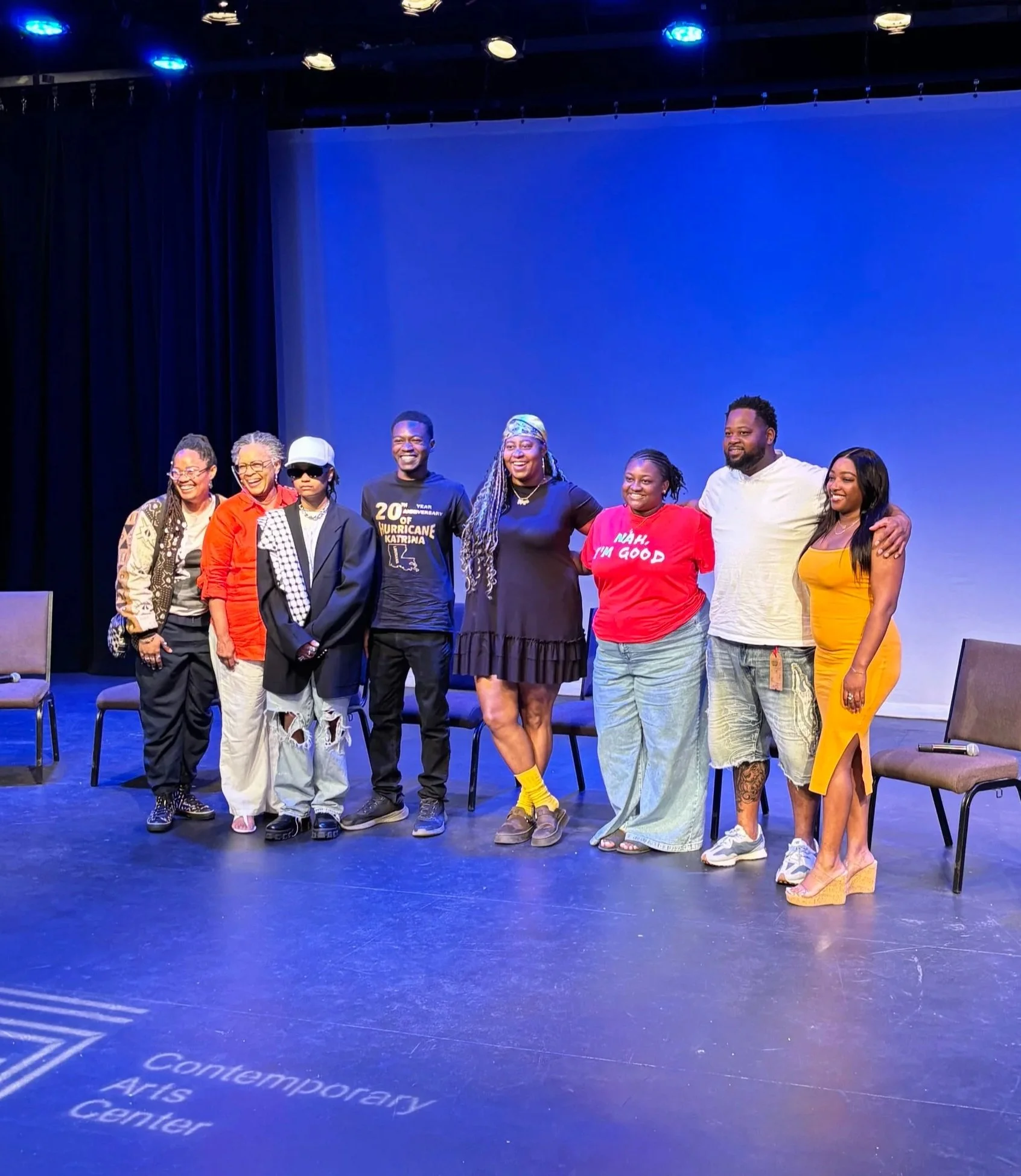 Group of nine Youth Stop Inc. student alumni standing on stage at the Contemporary Arts Center, smiling and posing for a photo.