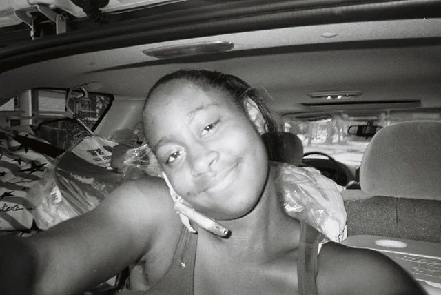 Young girl smiling inside a vehicle, with packages in the background.