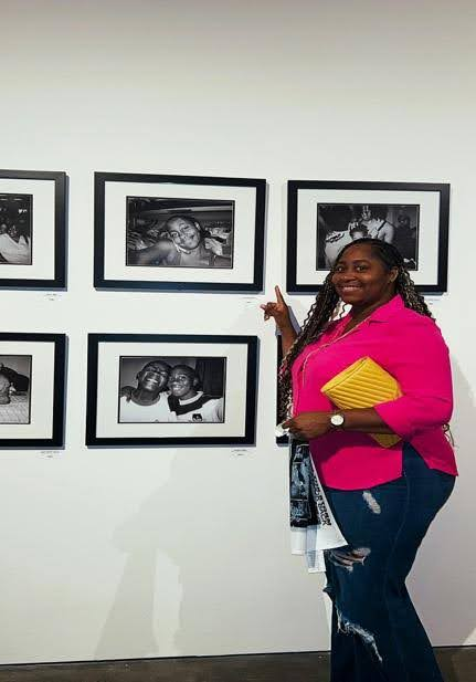 Woman in pink jacket pointing at framed black and white photographs on gallery wall