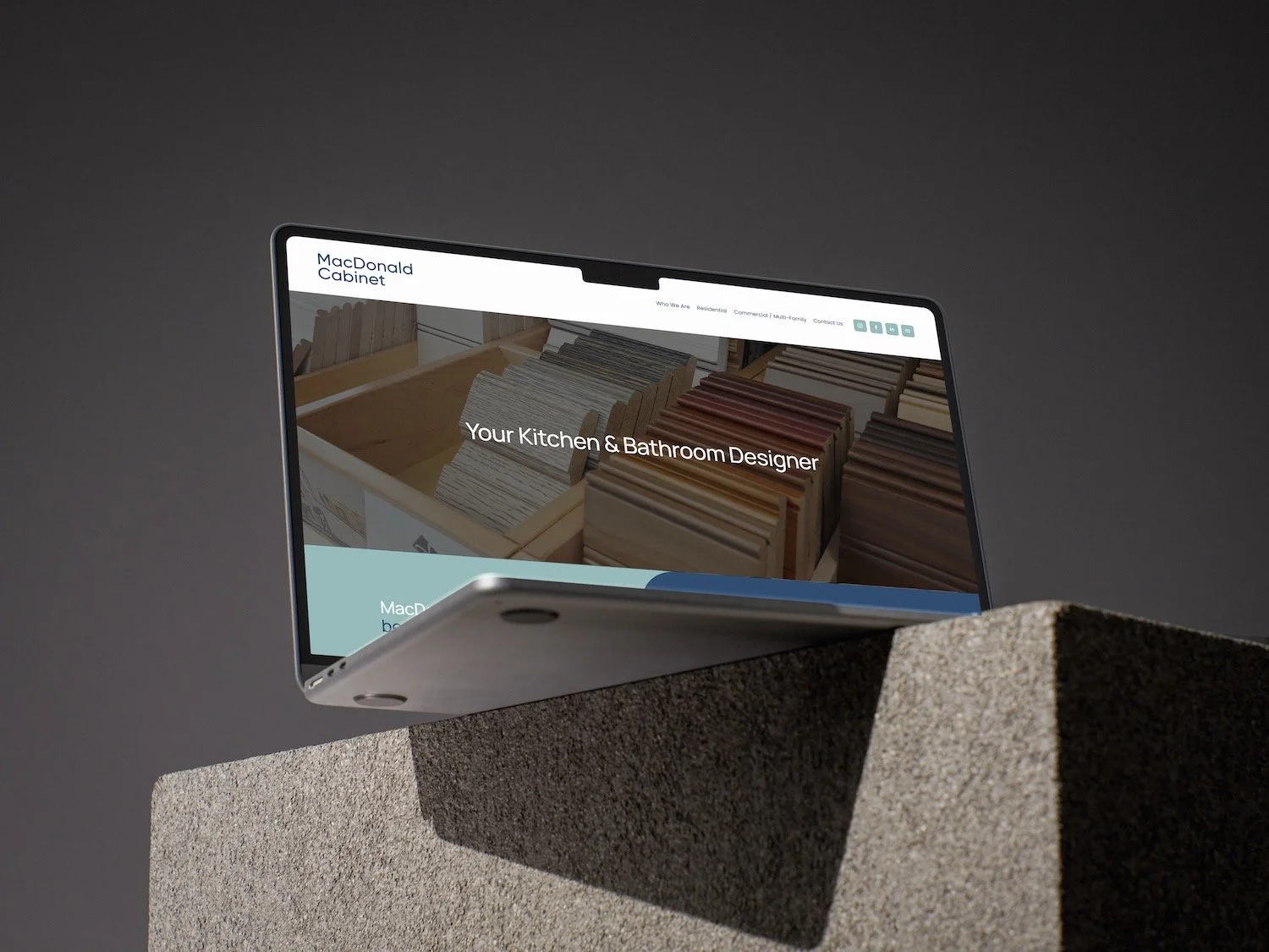 A sleek, modern tablet device resting on a concrete block displaying the website of MacDonald Cabinet, a kitchen and bathroom design company.
