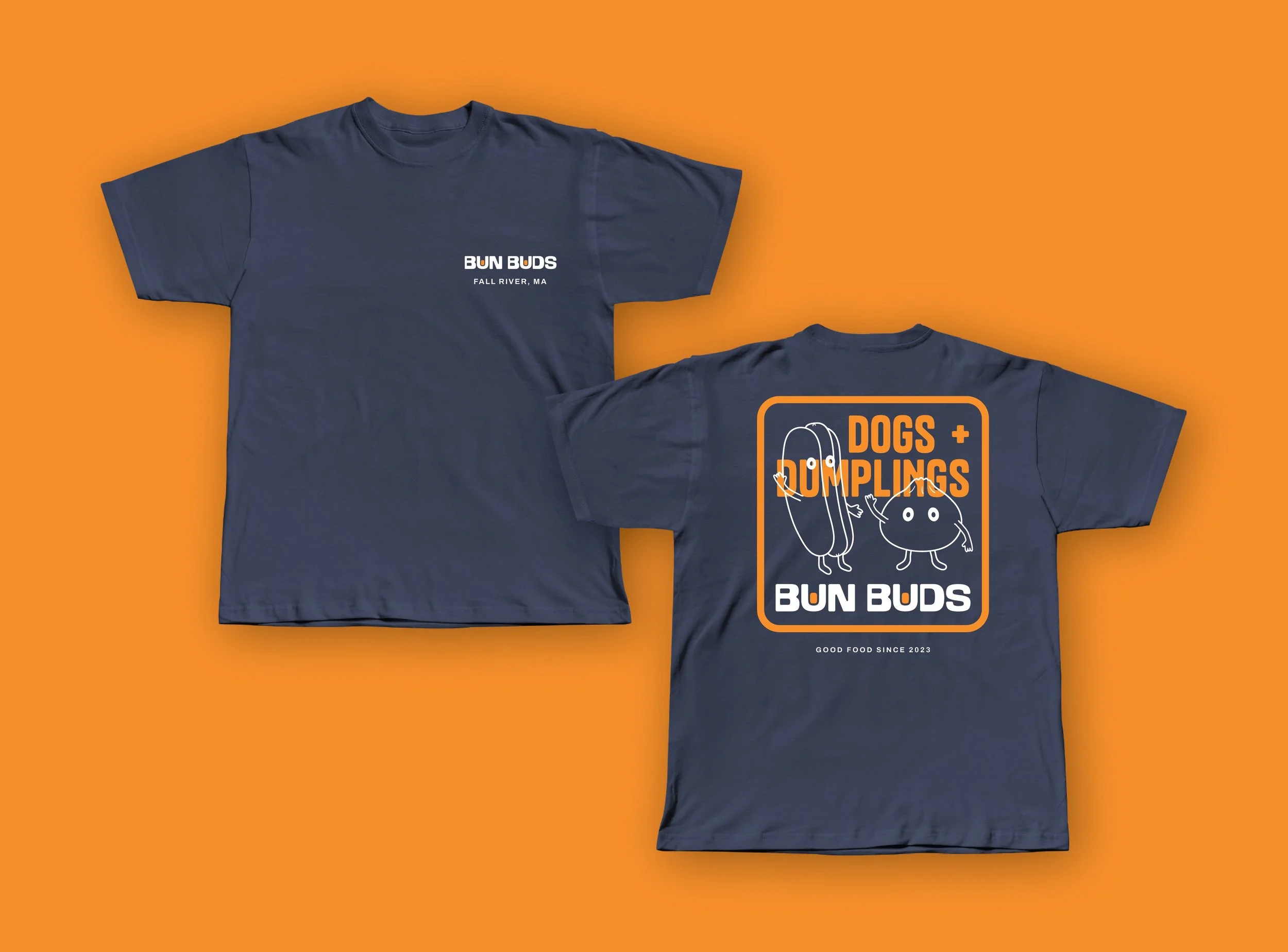 Two navy blue T-shirts on an orange background. The front of the left T-shirt reads "BUN BUDS FALL RIVER, MA". The back of the right T-shirt features a graphic with cartoon hot dogs and buns, and the text "DOGS + DUMPLINGS" and "BUN BUDS".