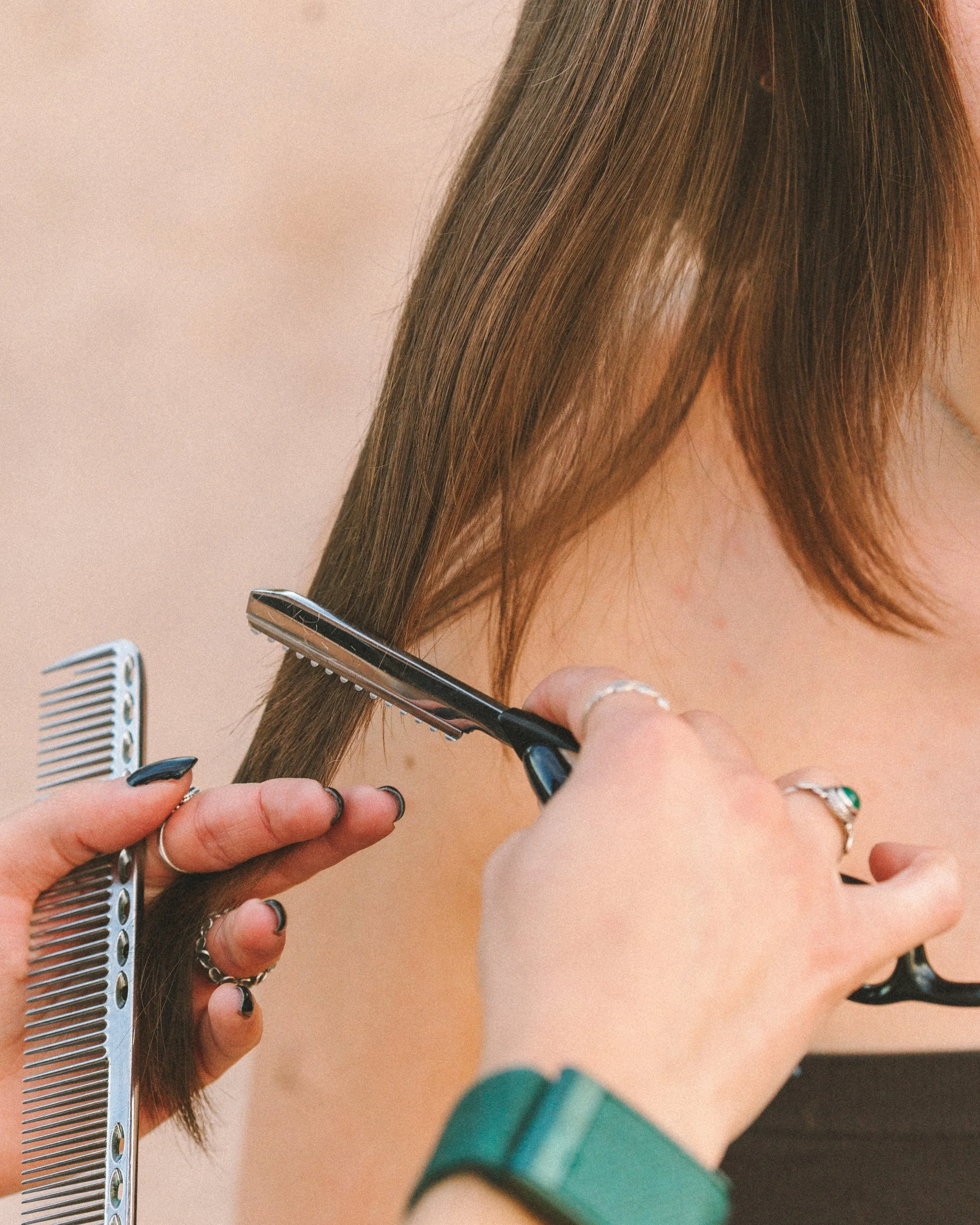 A person is cutting a woman's brown hair with scissors while holding a comb and a section of hair.