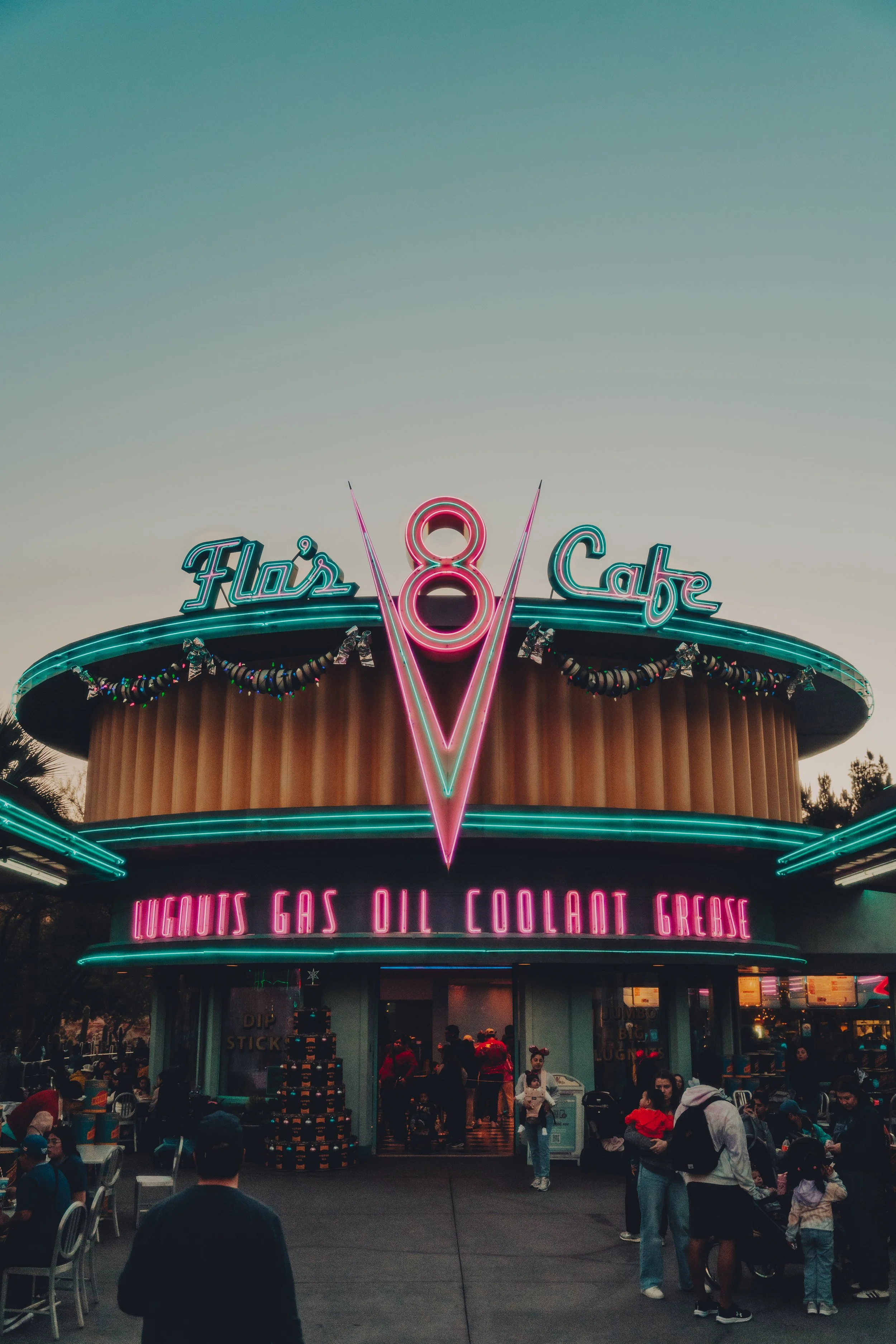 Neon-lit retro diner named Flo's Cafe with neon signs and people outside.