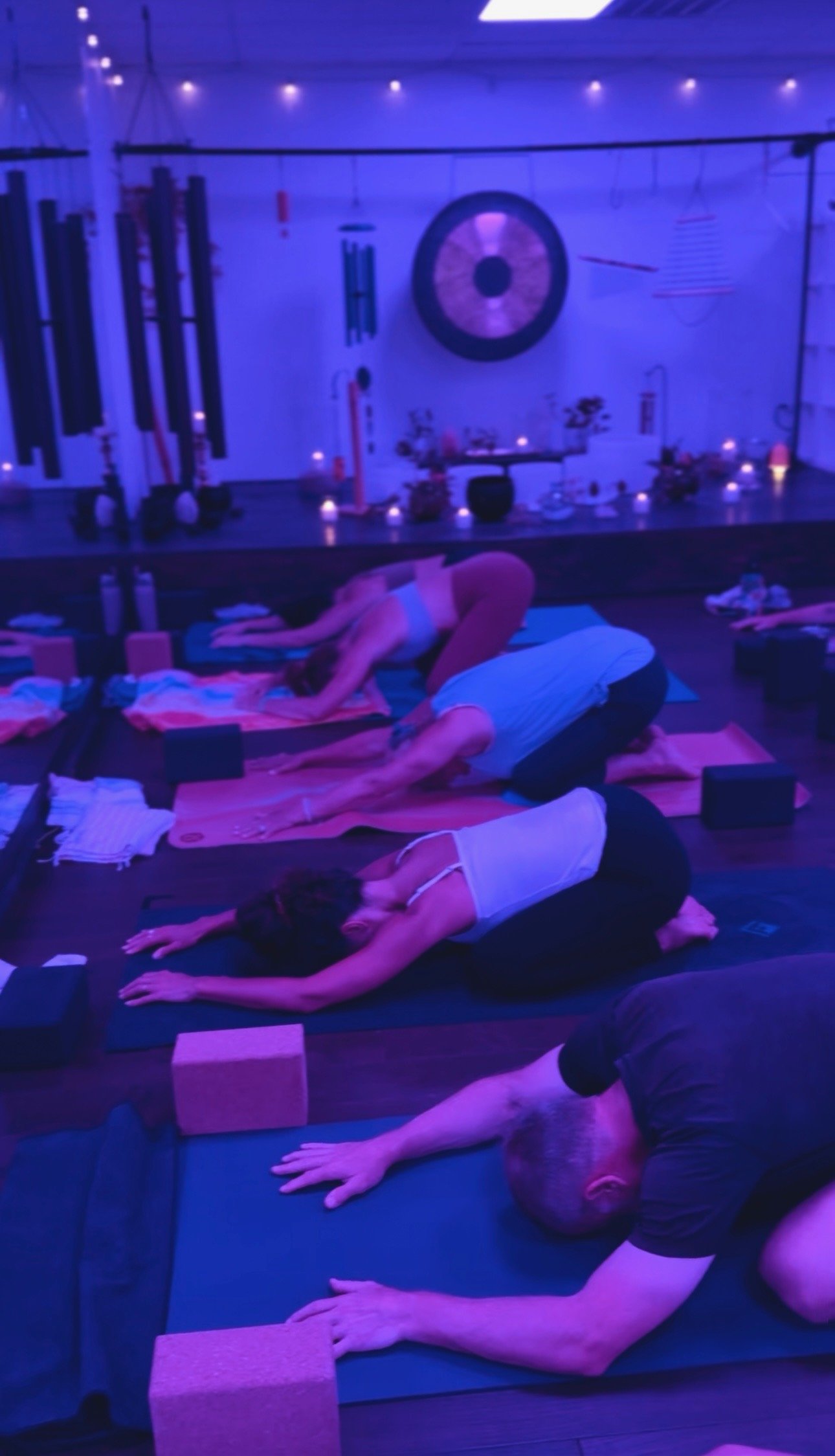 People practicing yoga in a dimly lit room with blue lighting, using yoga mats and blocks.