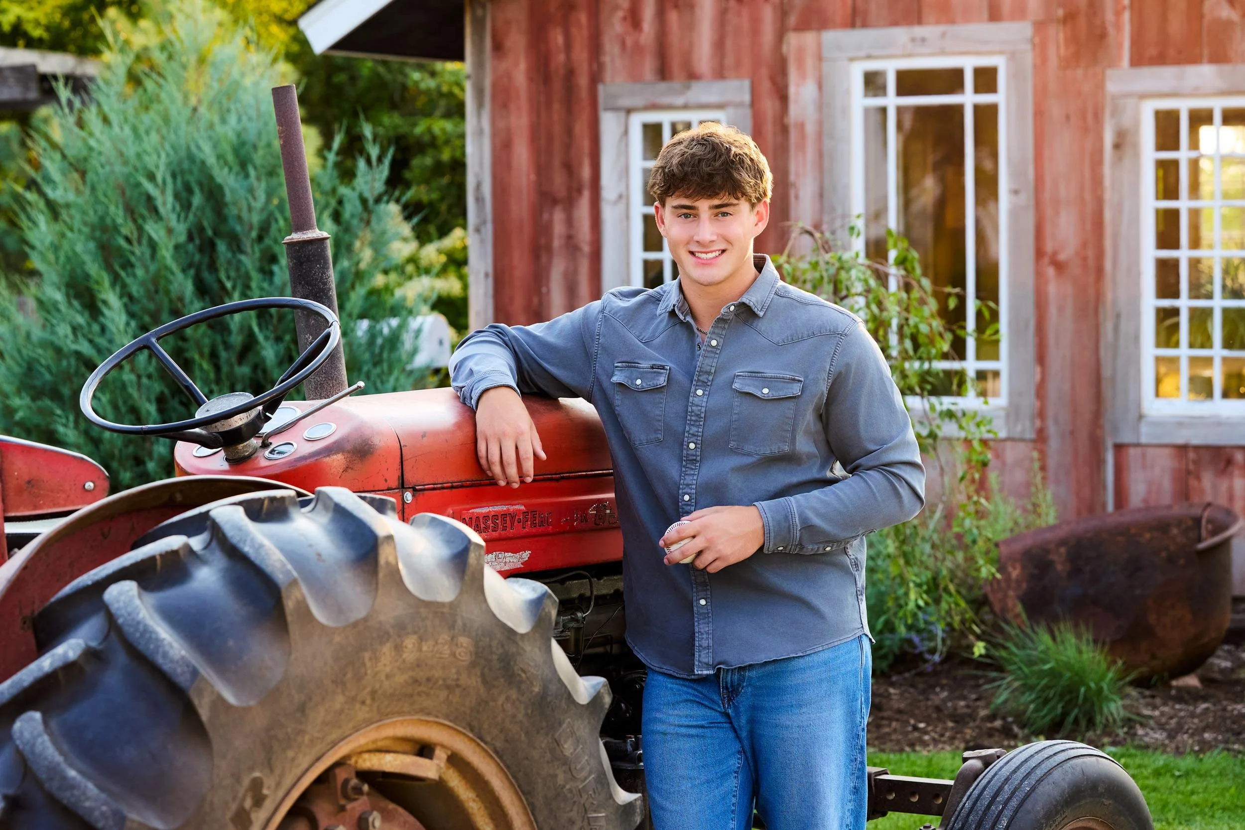 High school senior holds baseball and leans on his grandfather's red tractor near Rochester MN