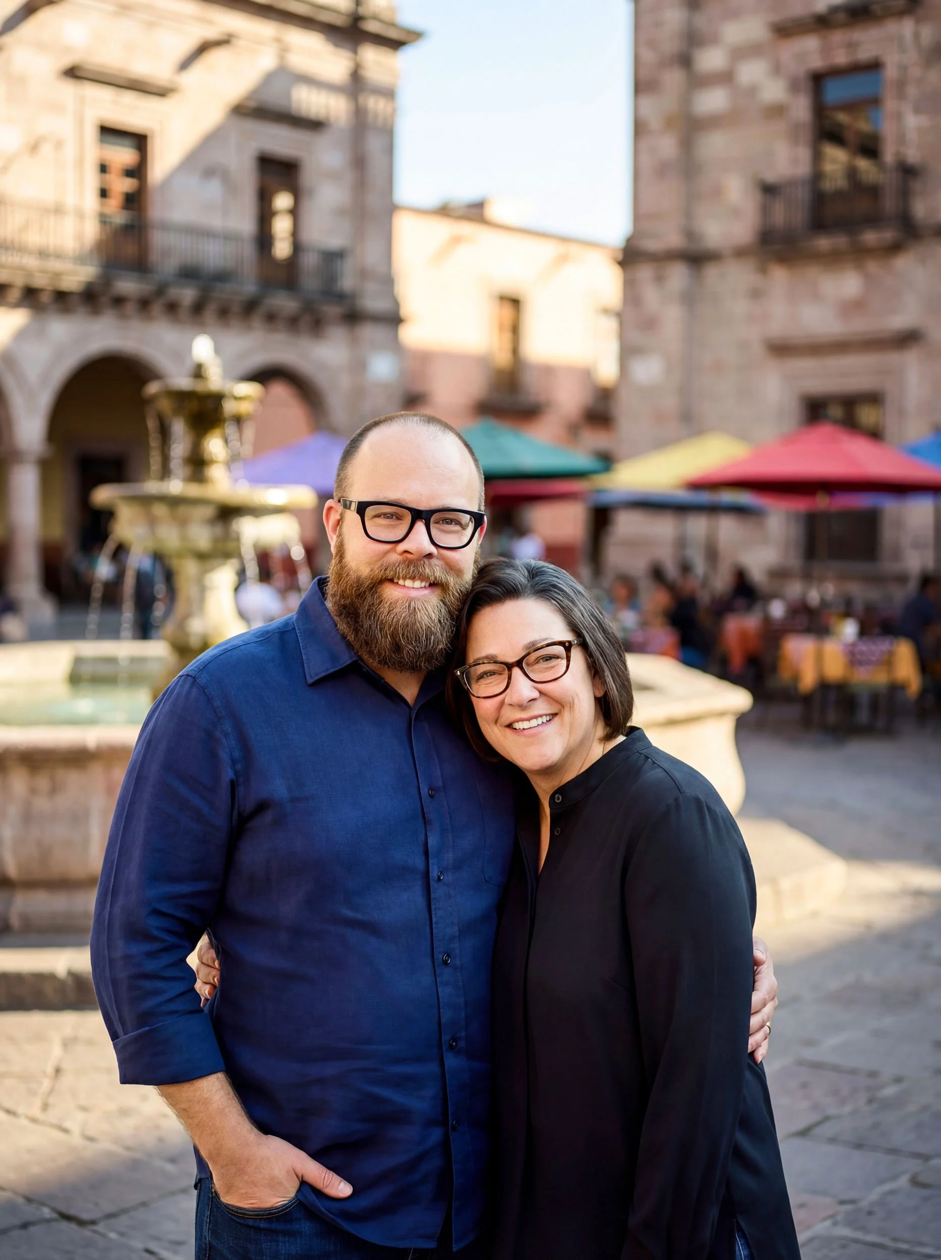 man and woman standing in front of fountain in Europe plaza with fountain. man has around around woman's waist and she is resting head on his shoulder. both are smiling at camera.