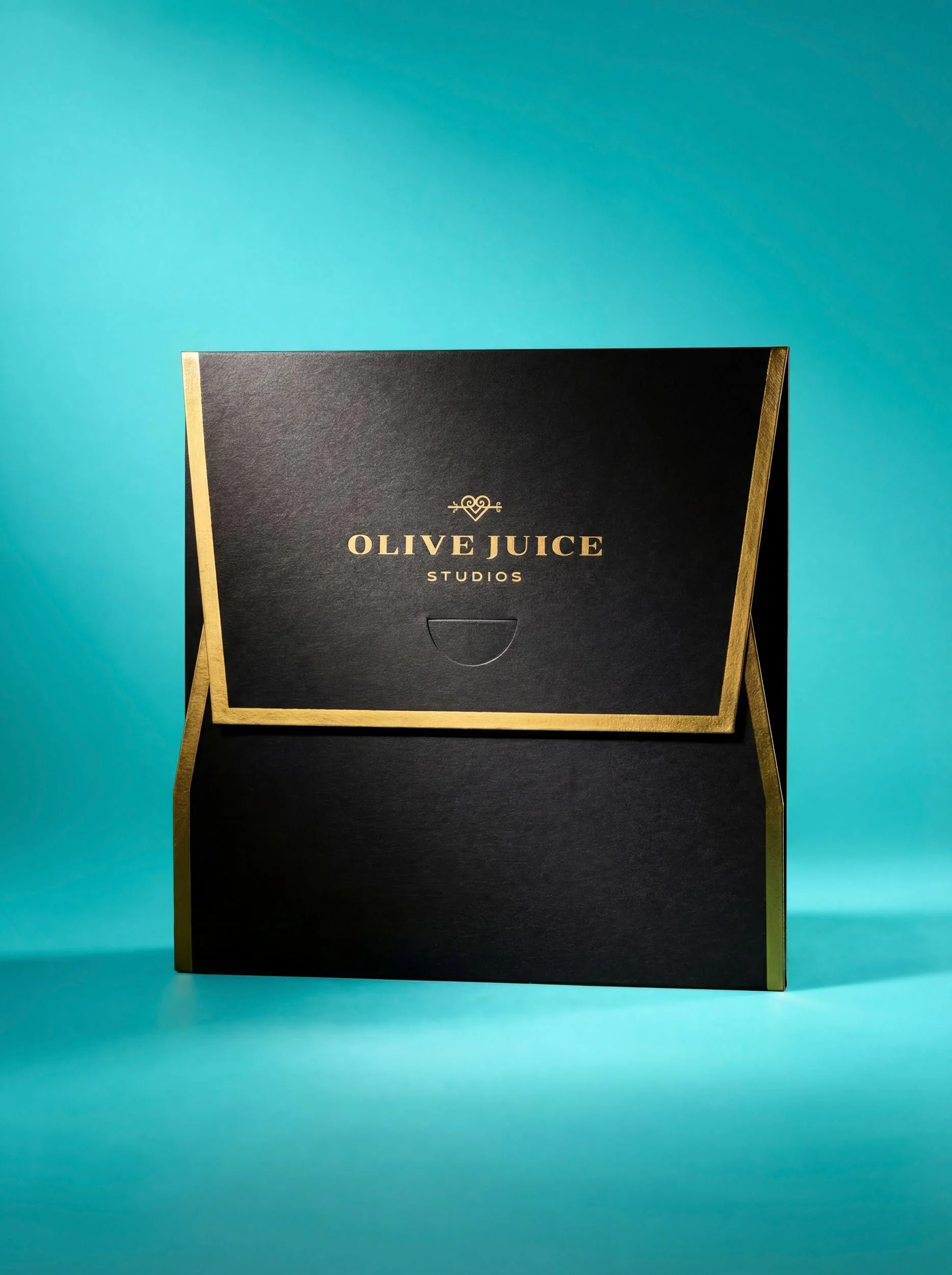 square matte black envelope with gold foil edges. top flap has words olive juice studios and heart logo