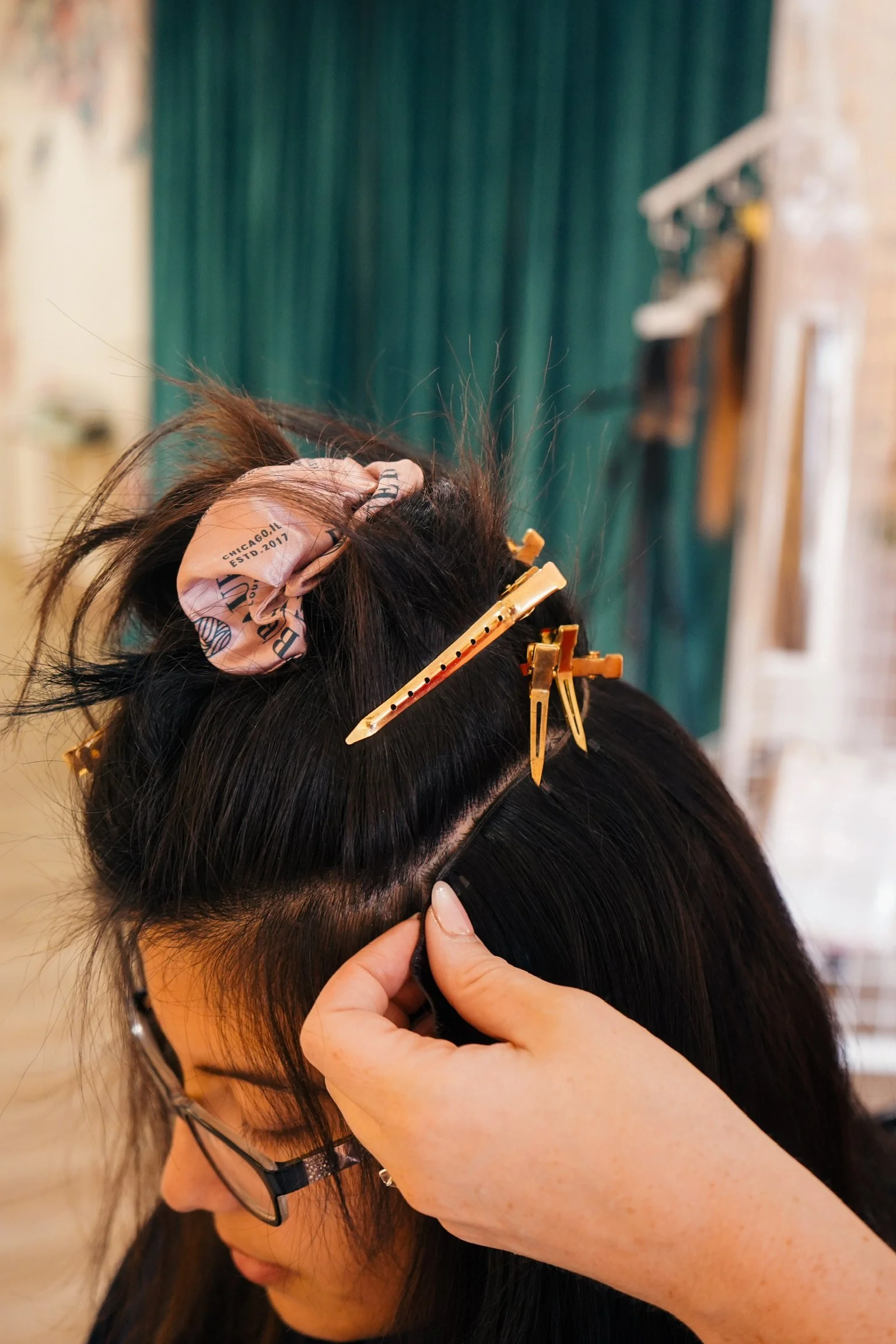 A person getting their hair styled, with hair clips and a scrunchie in their black hair, in a salon setting.
