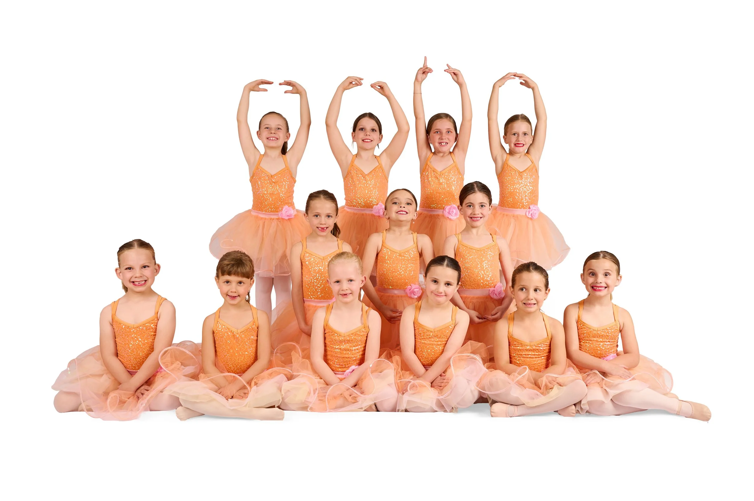 Group of young girls and an instructor jumping and dancing outdoors in a field, wearing black dance clothes, with trees in the background, and a Virtuosity Dance Centre logo in the lower right corner.