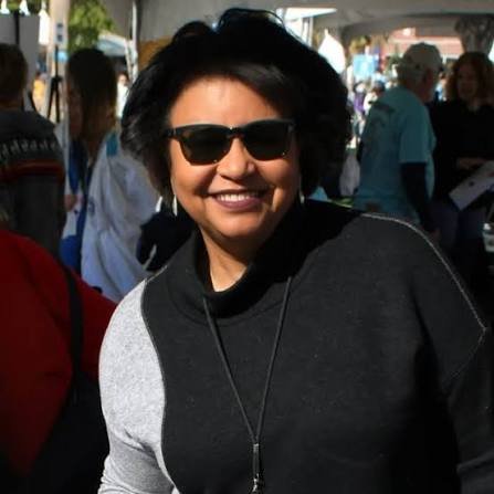 Author Wanda Penalver Bevan smiling outdoors, wearing sunglasses and a black-and-gray top.