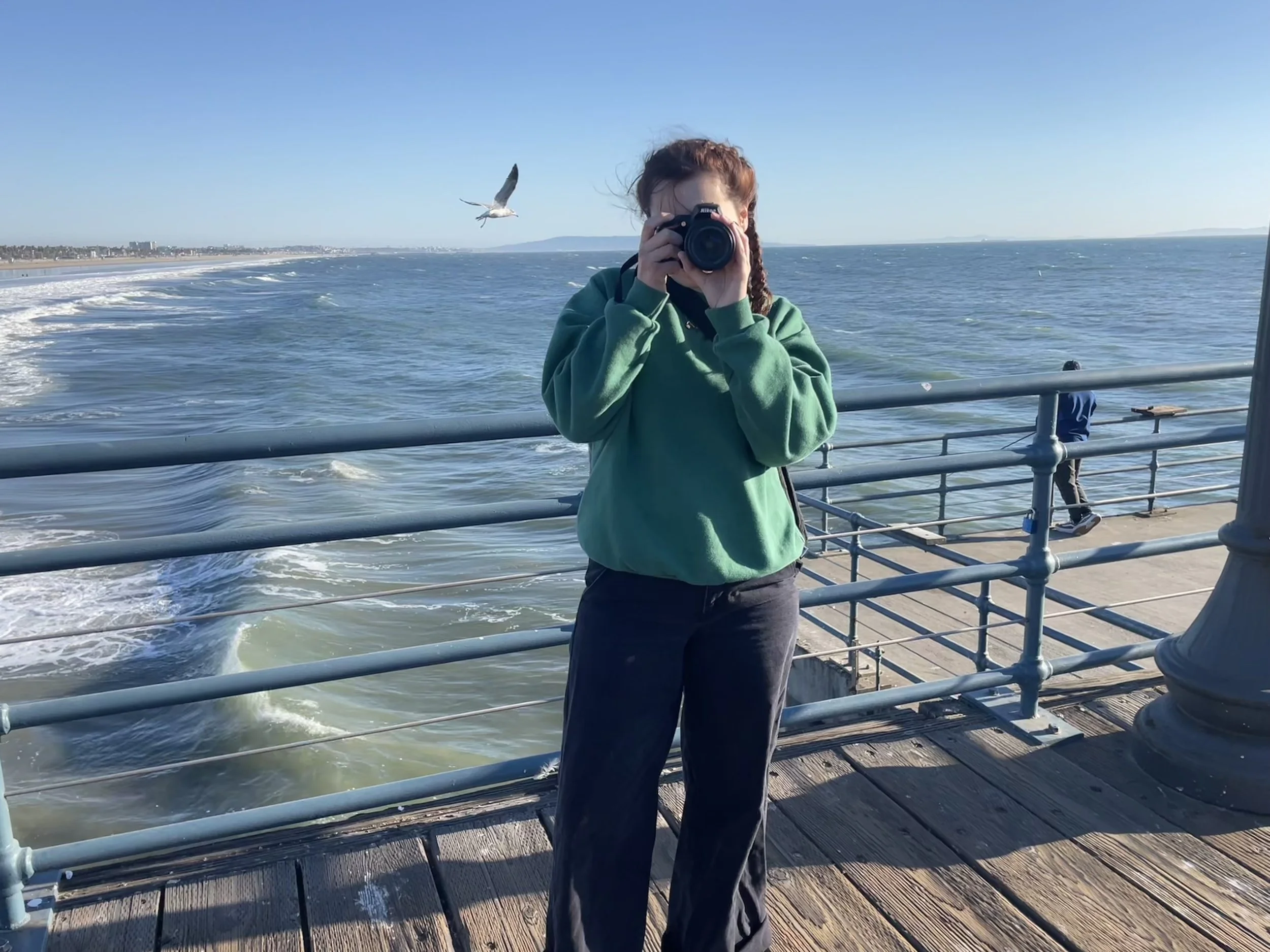 Woman taking a photo with a camera on a pier overlooking the ocean.
