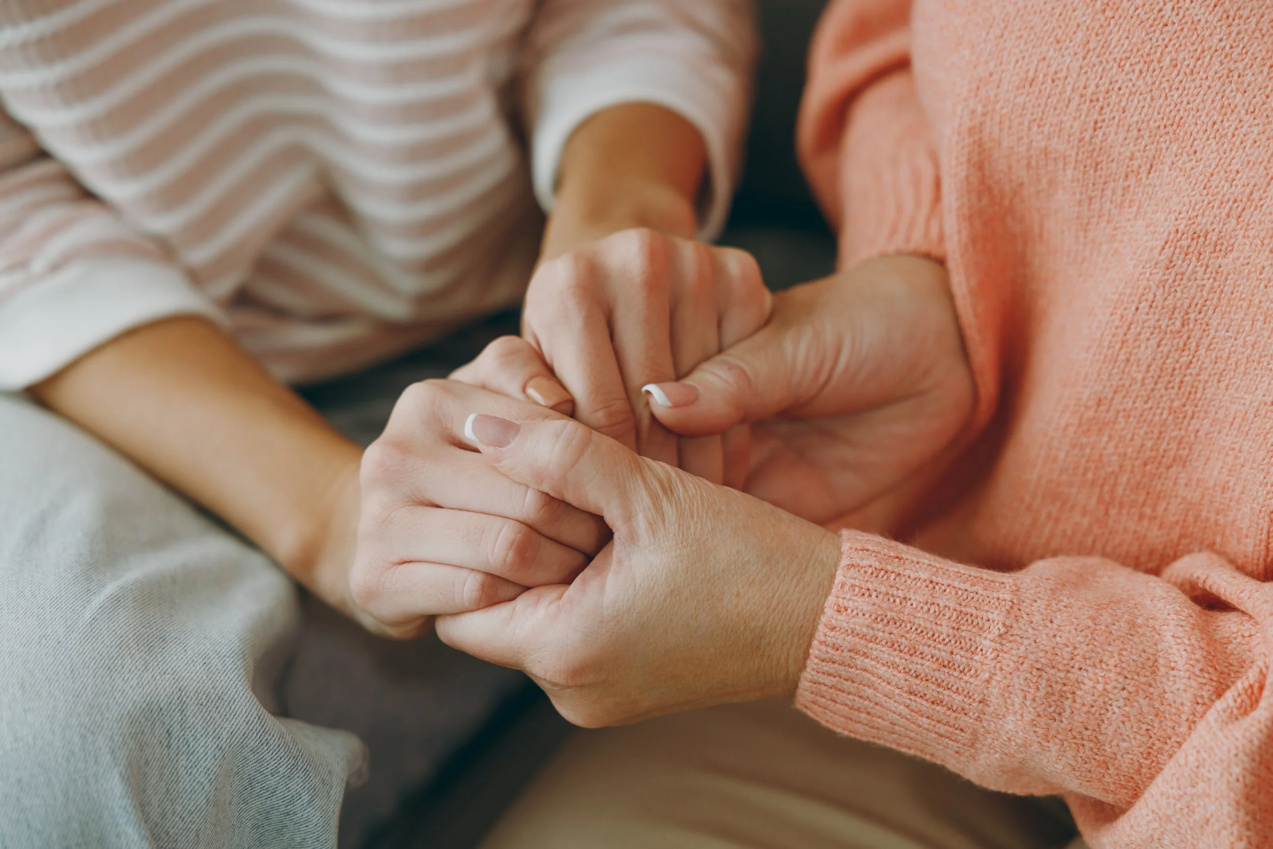 Two women hold hands out of support.