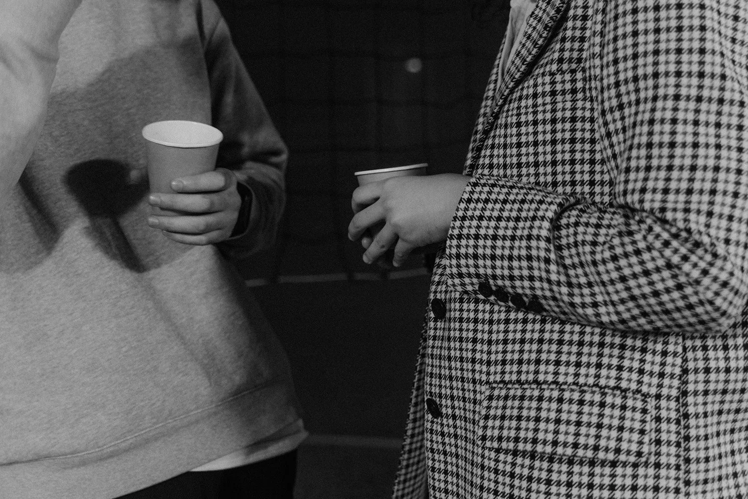 two people facing each other holding paper cups, presumably coffee.