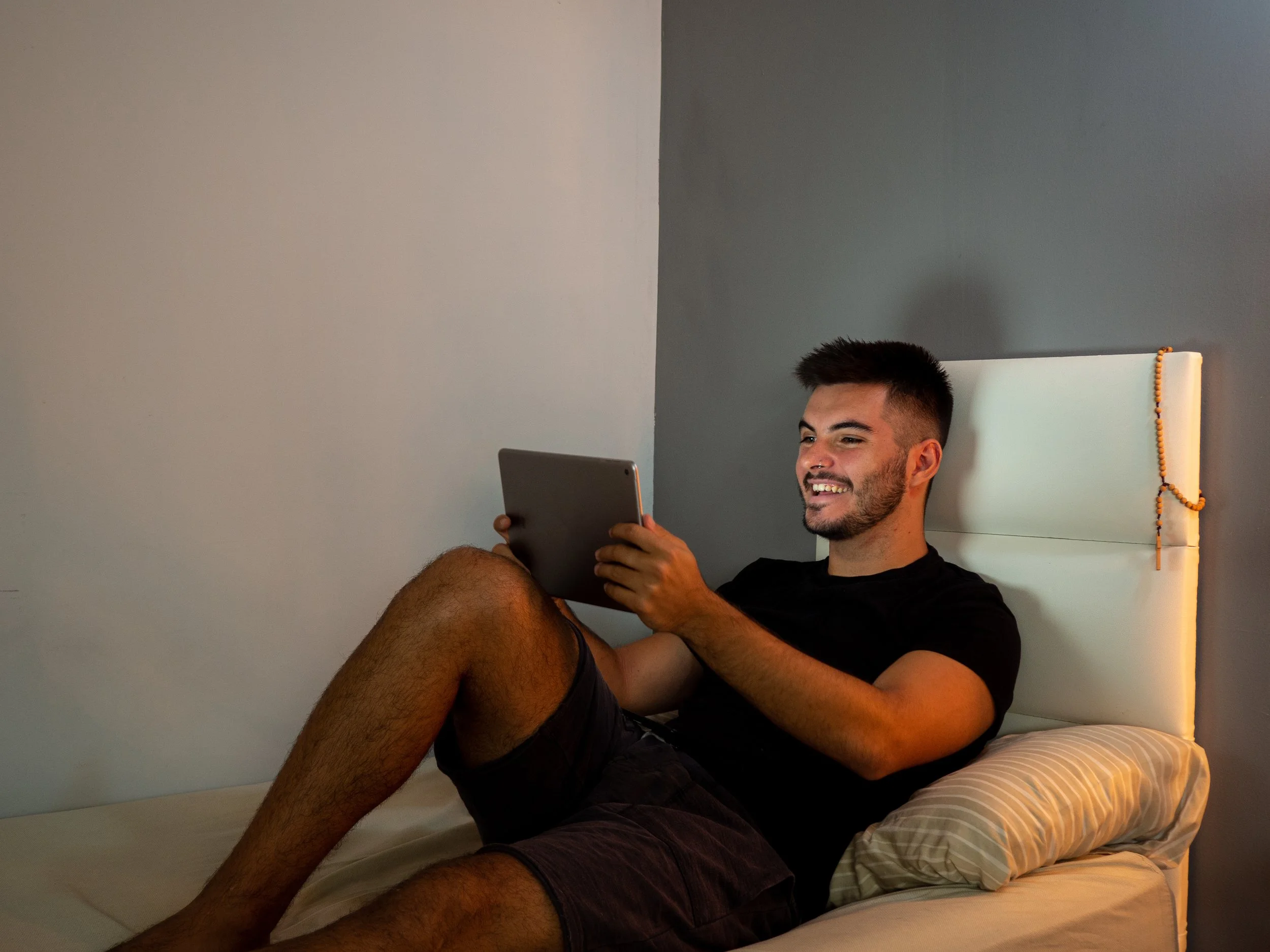 A man on his bed uses his tablet to video chat.