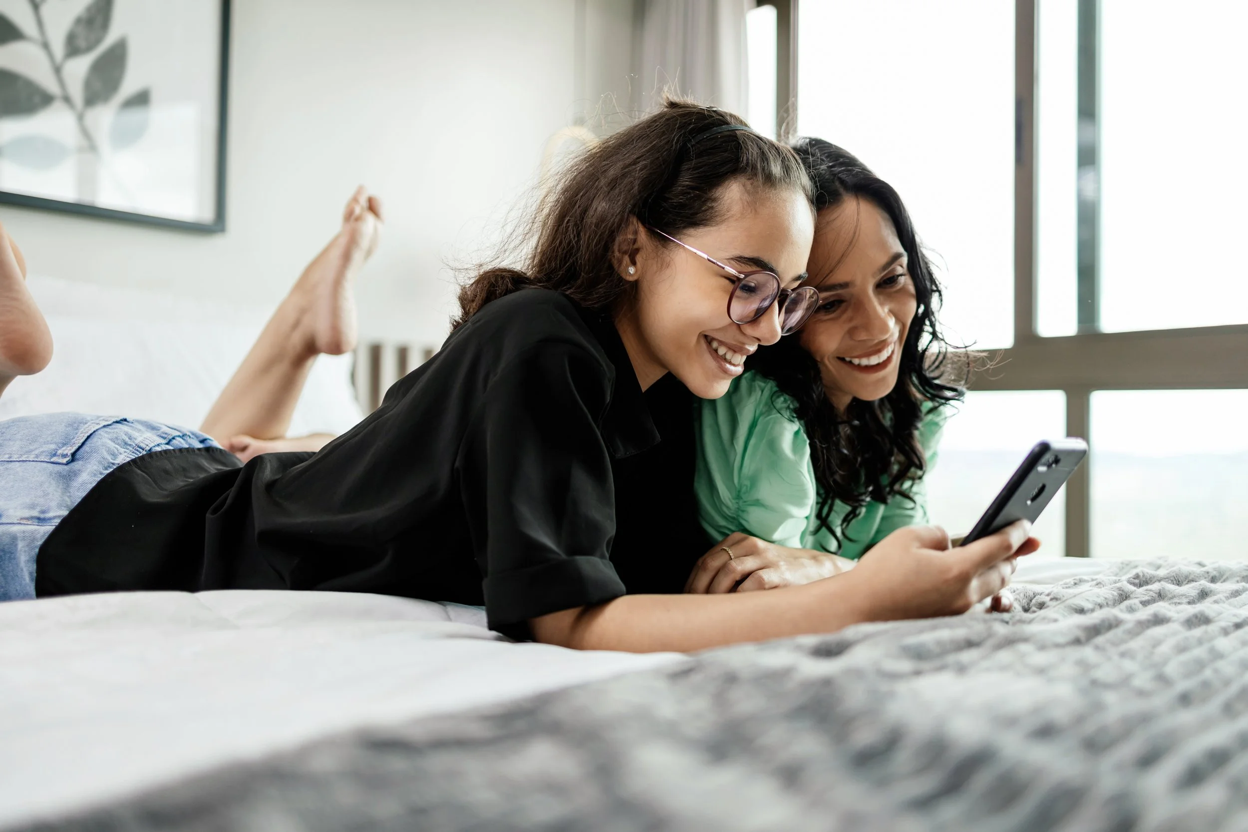 Two girls lay down on bed and use phone.
