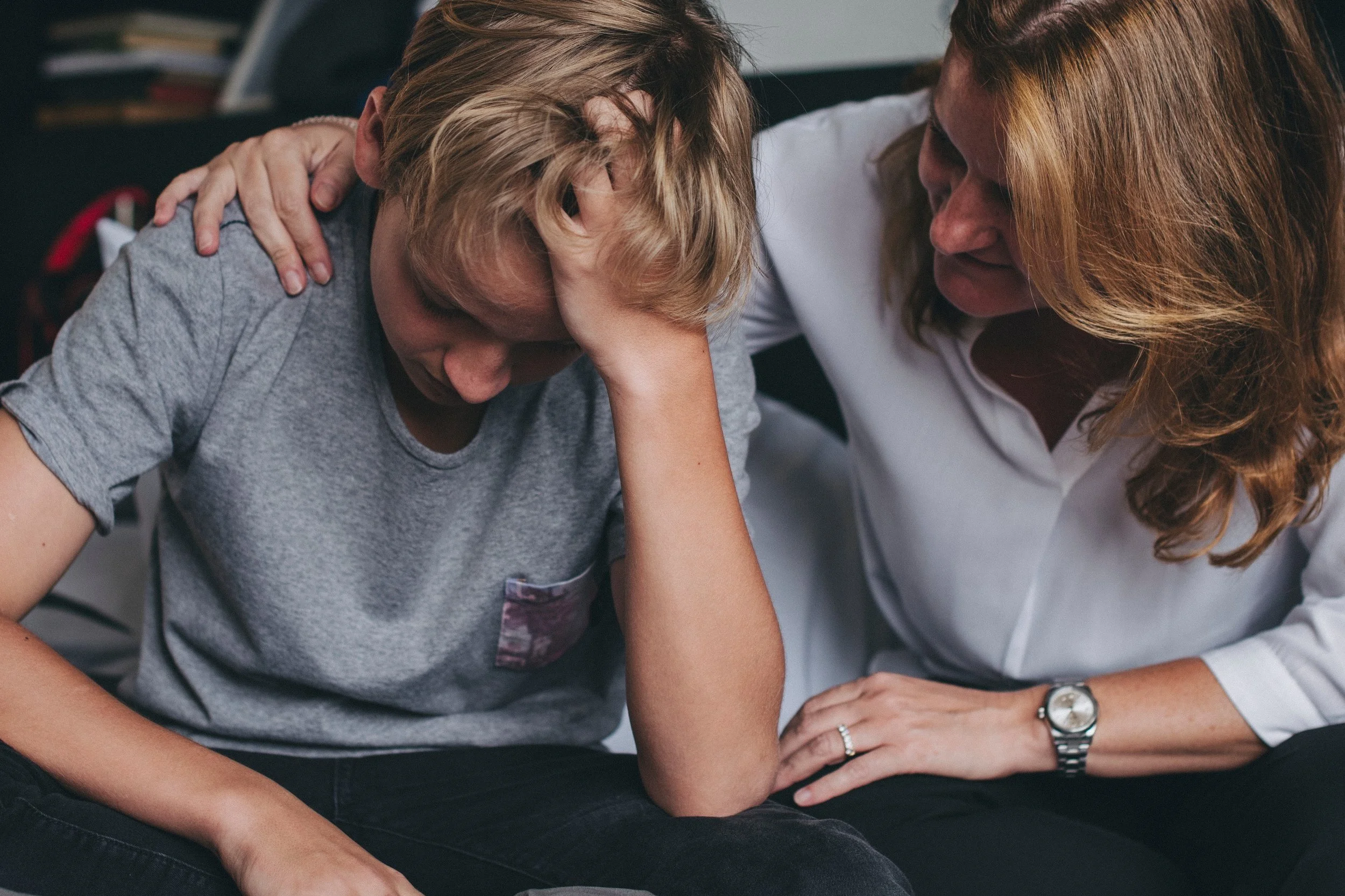 A teenager has his hand in his head looking down while an adult comforts him by touching his shoulder.