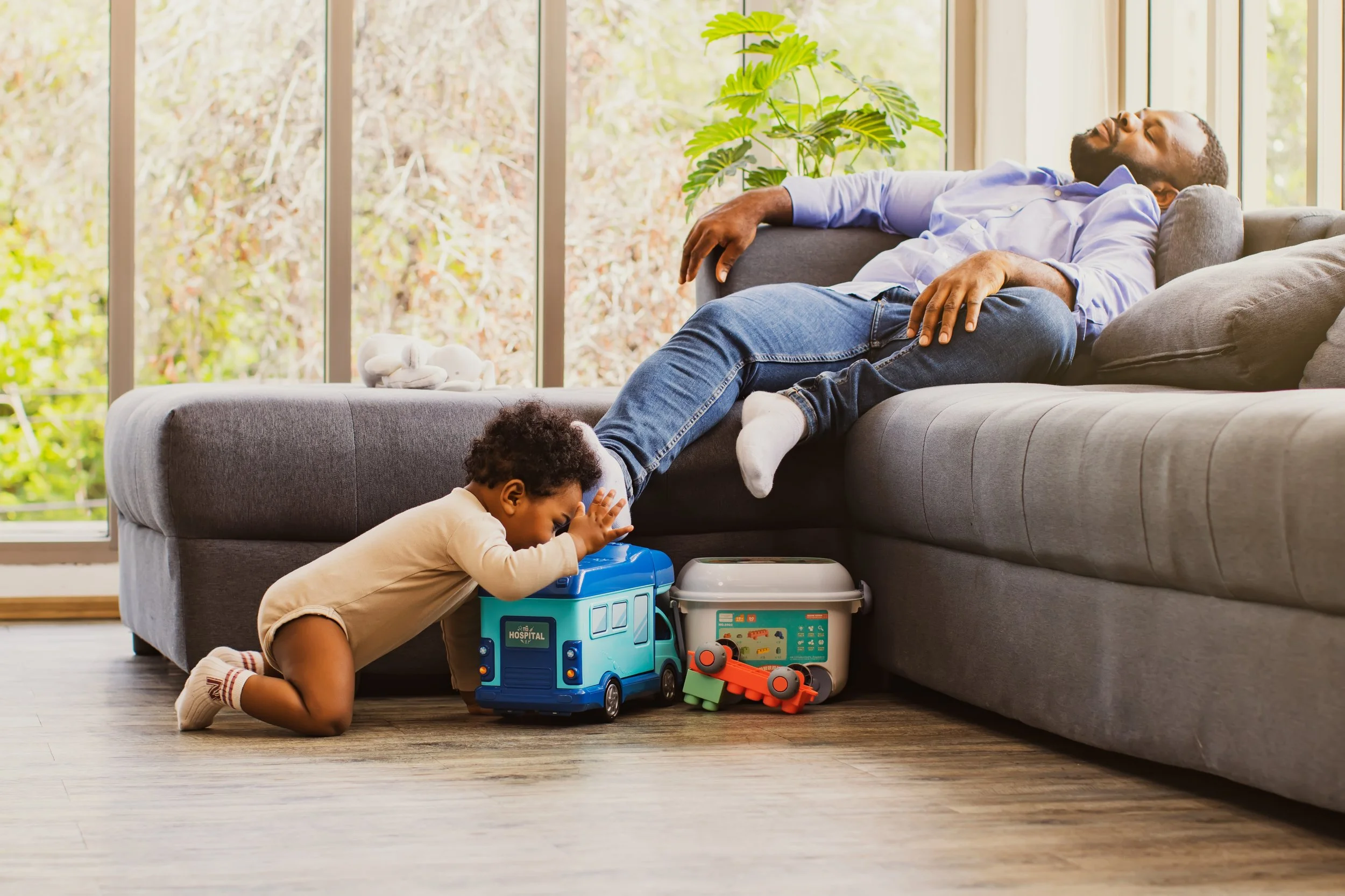 A father sleeps on the couch instead of taking care of his toddler.