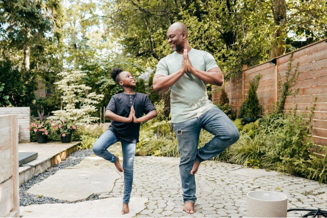 father and child standing in a yoga pose outside, looking at each other with smiles