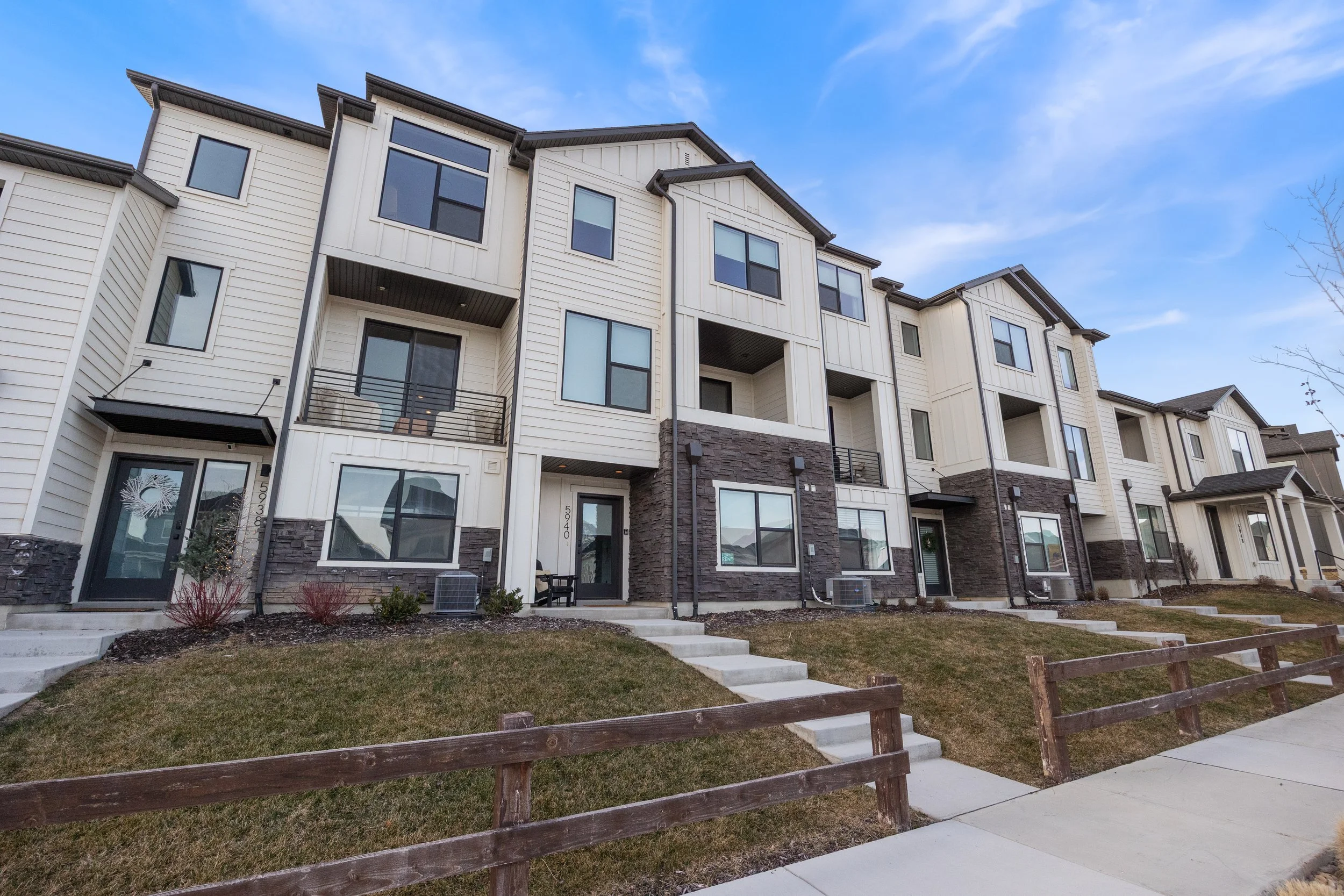 Exterior view of modern townhouses with multiple stories, large windows, and small balconies, under a clear blue sky.